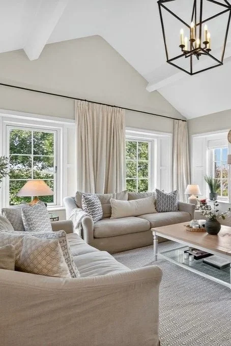 Bright living room with white sofas, beige curtains, side lamps, and a geometric pendant chandelier hanging from the ceiling.