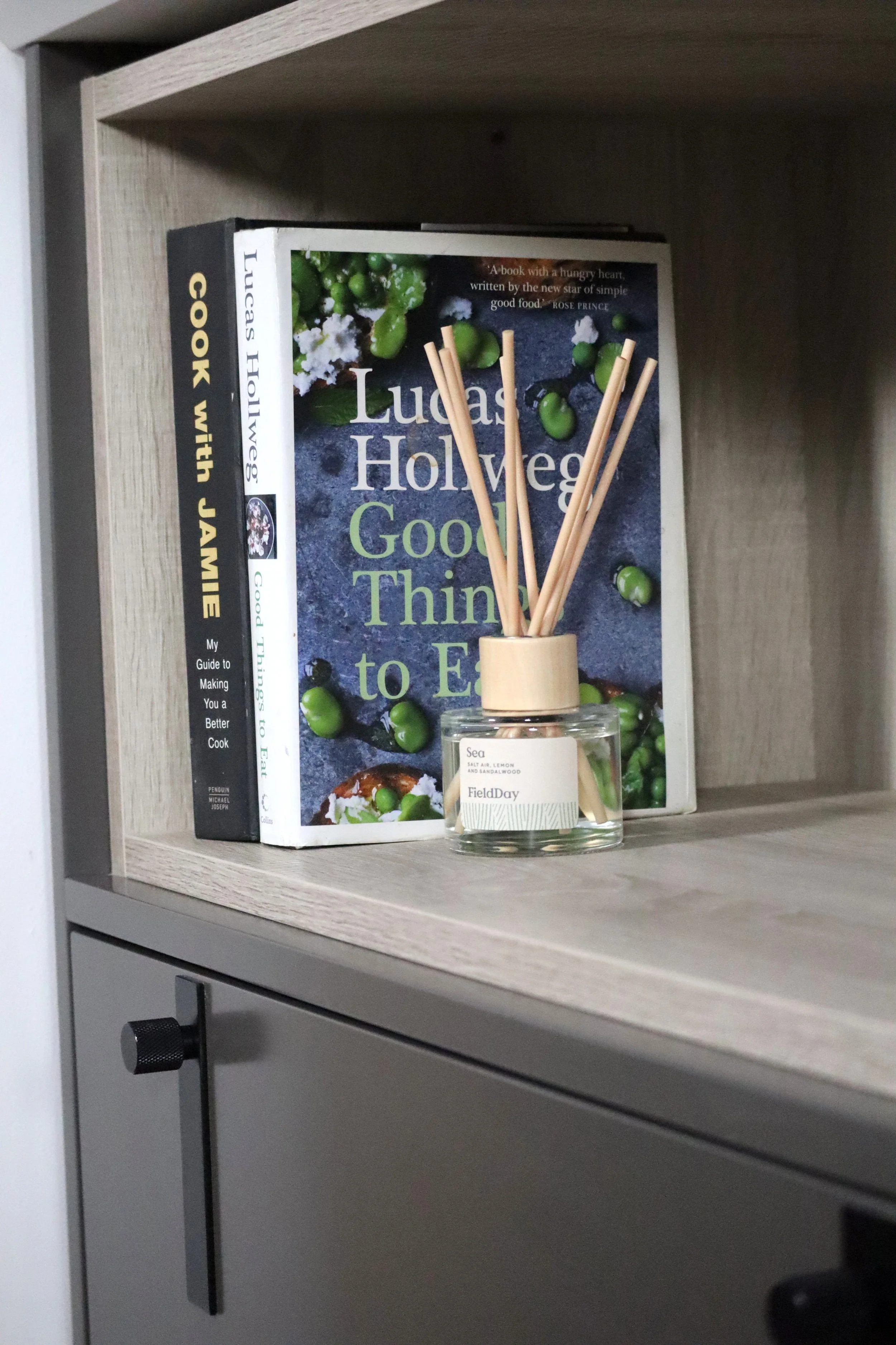 Bookshelf with a cookbook titled "Good Things to Eat" by Lucas Holweg, a reed diffuser labeled "Sea..." and a room key or label from FieldDay.