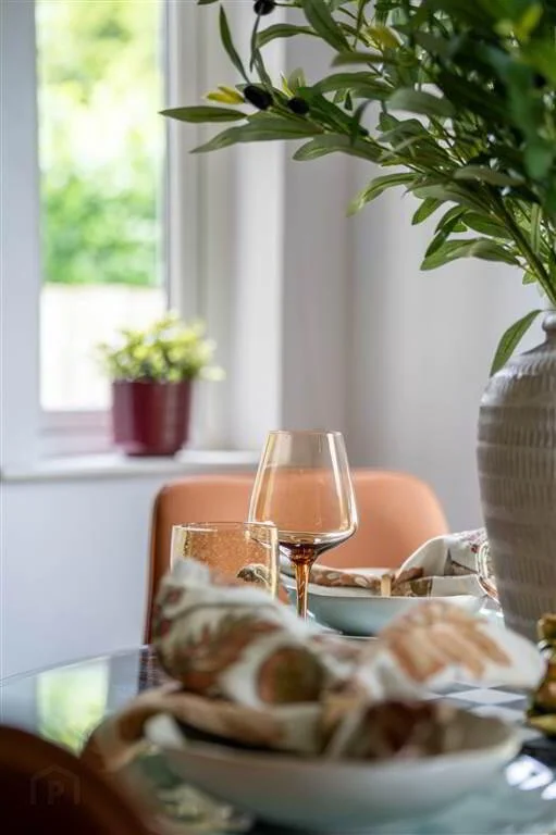 A dining table with a glass of water and a wine glass, with a plate of appetizers, in a room with a window and a potted plant in the background.