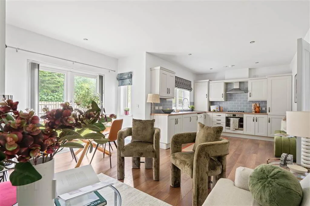 Open living room and kitchen with white cabinetry, hardwood floors, and large window with greenery outside.