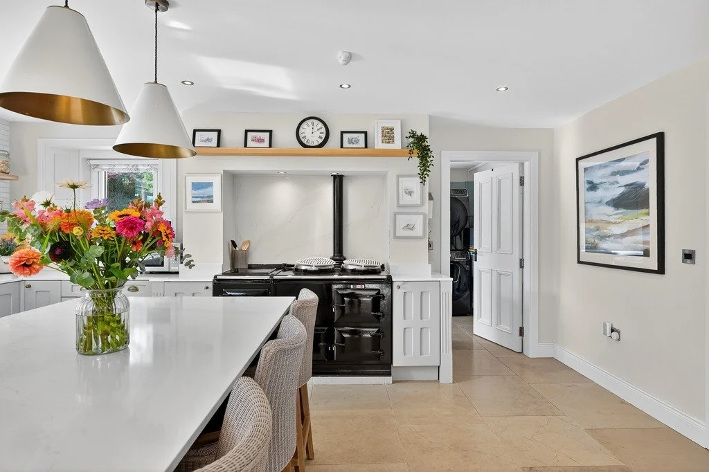 A bright kitchen with white cabinets, a black stove, and a white dining table with a vase of colorful flowers.