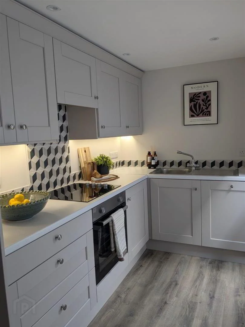 Modern kitchen with white cabinets, black and white geometric backsplash, black stovetop, gray flooring, and framed wall art.