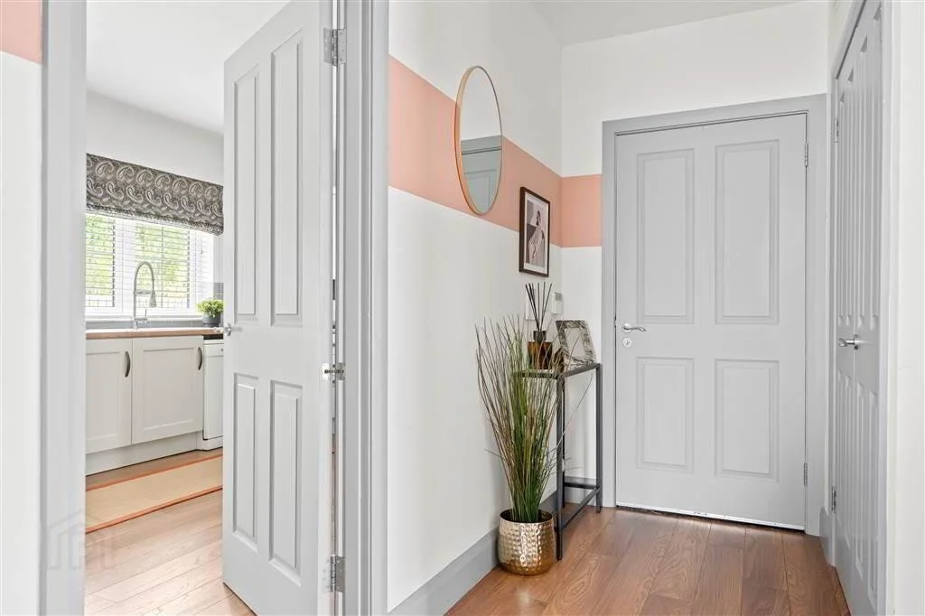 Entryway with white door, decorative side table with plant and framed photos, wall mirror, and photo frames, with a view into the kitchen.