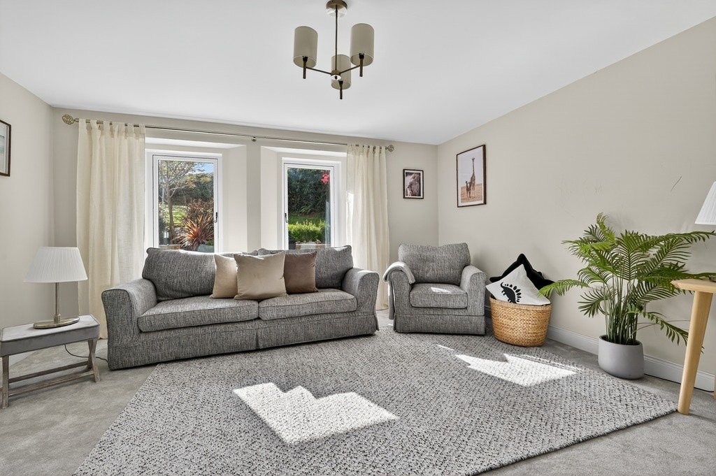 Bright living room with grey sofa and armchair, white curtains, potted plant, wall art, and a light-colored rug.