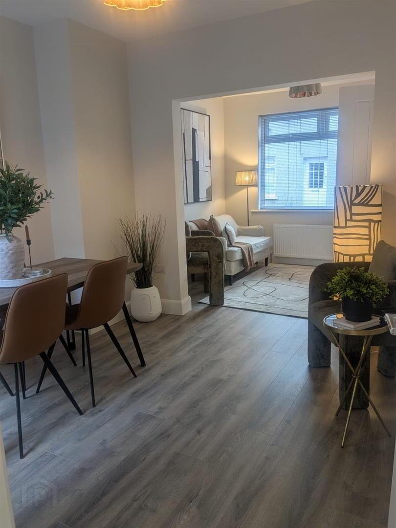 Living room with a dining table and chairs, a sitting area with a sofa and armchair, a large window, and modern decor including plants, lamps, and abstract artwork.