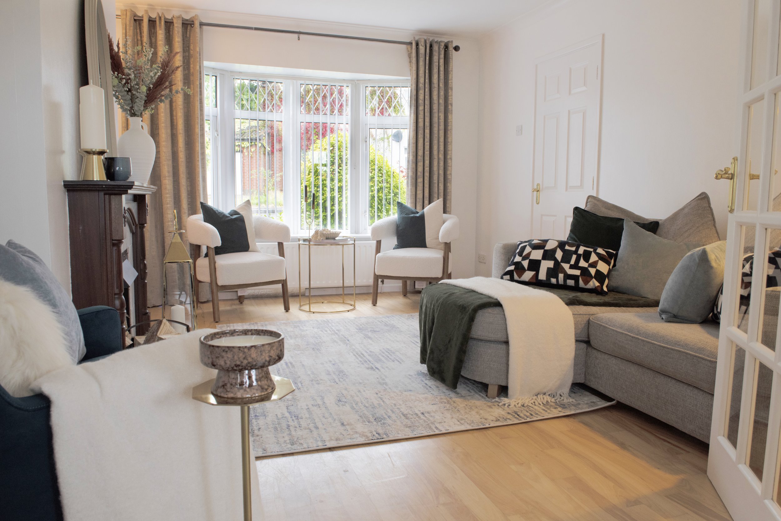 Bright living room with large bay window, white and gray furniture, decorative pillows, and a wooden floor.