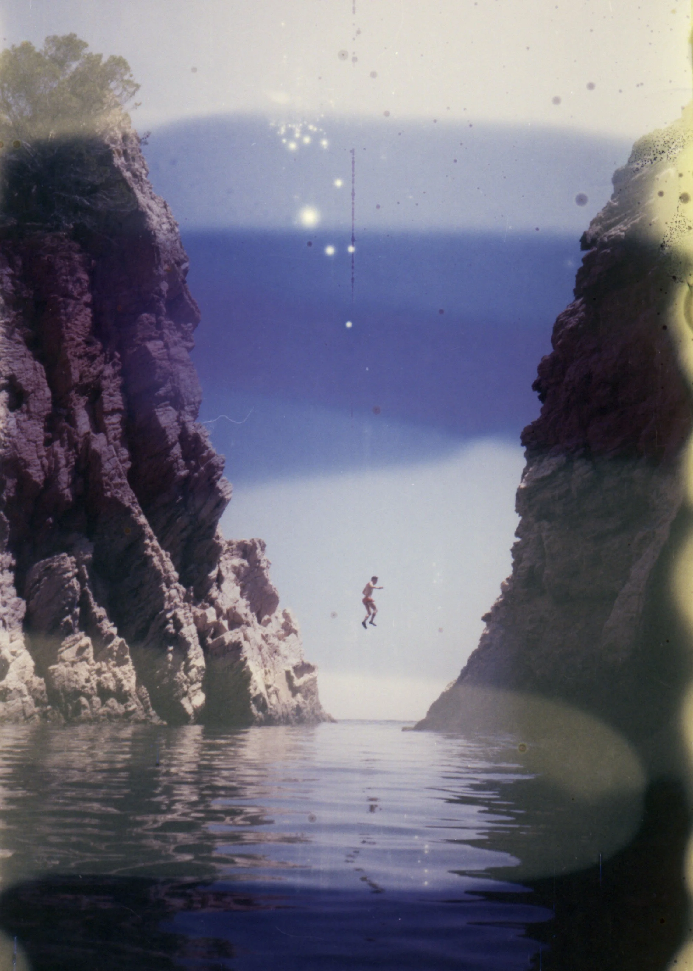 Persona saltando entre dos acantilados sobre agua, con fondo de cielo y mar.