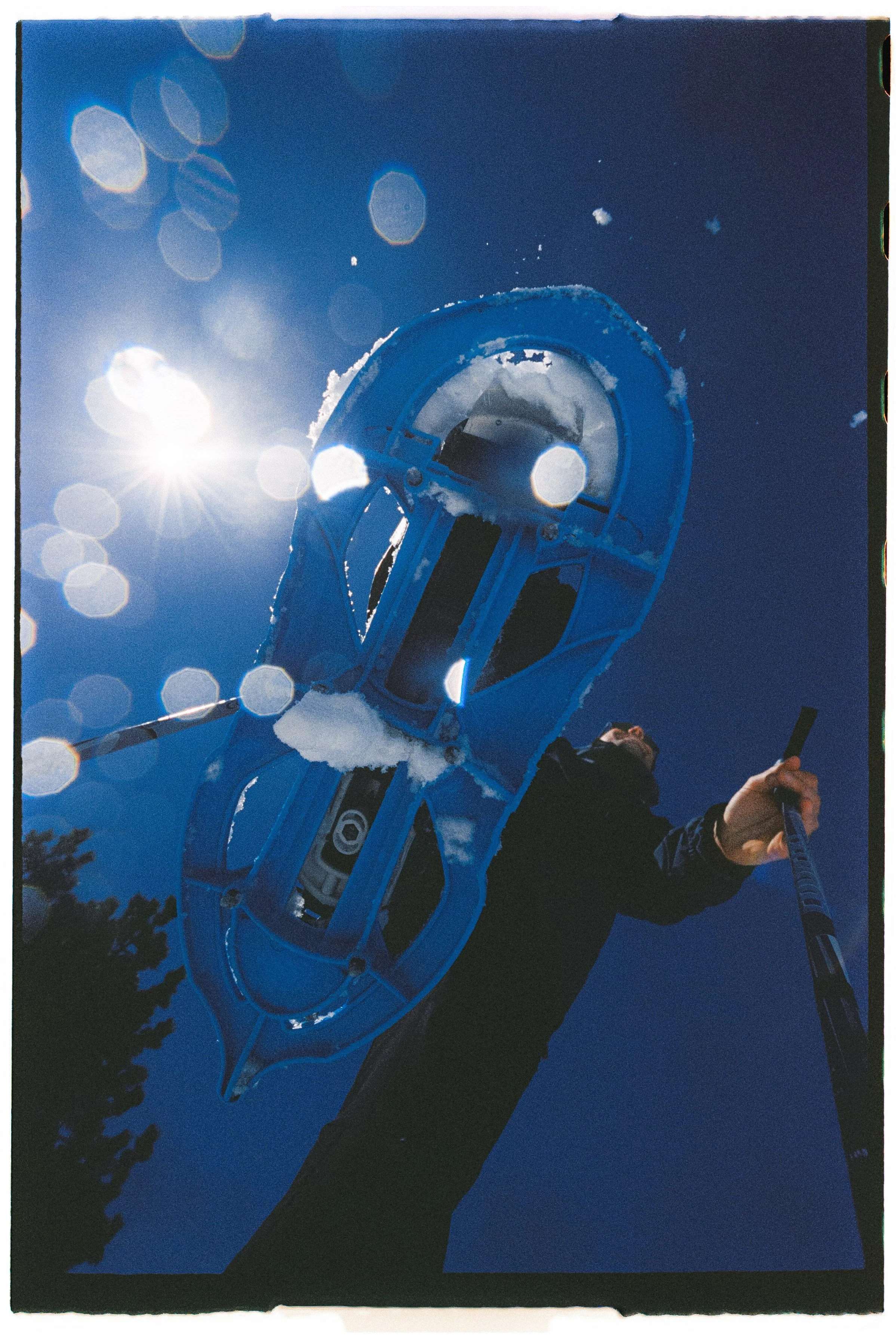 Persona sosteniendo un raquero de hielo en un día soleado con cielo azul y nieve en el suelo.