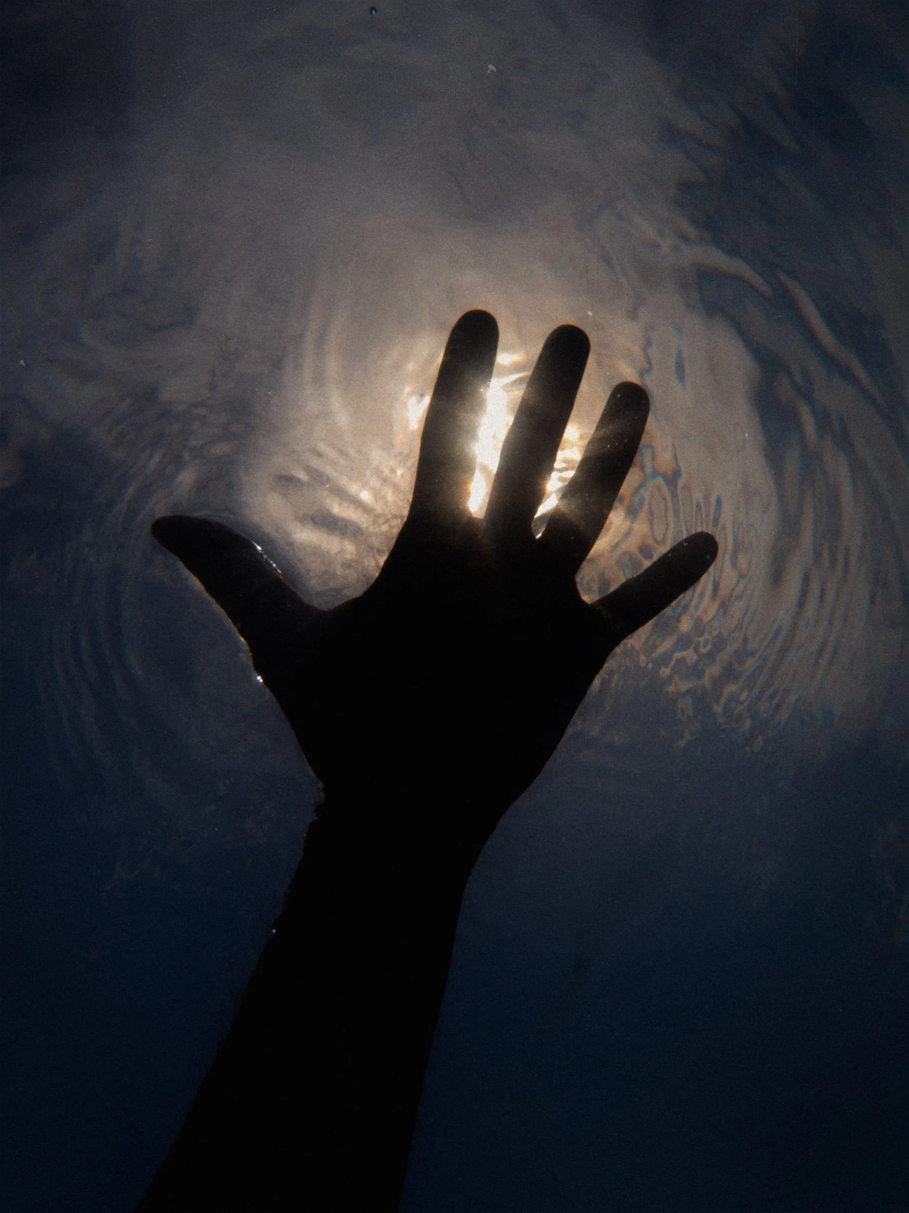 Mano sumergida en agua con luz solar reflejándose en la superficie.