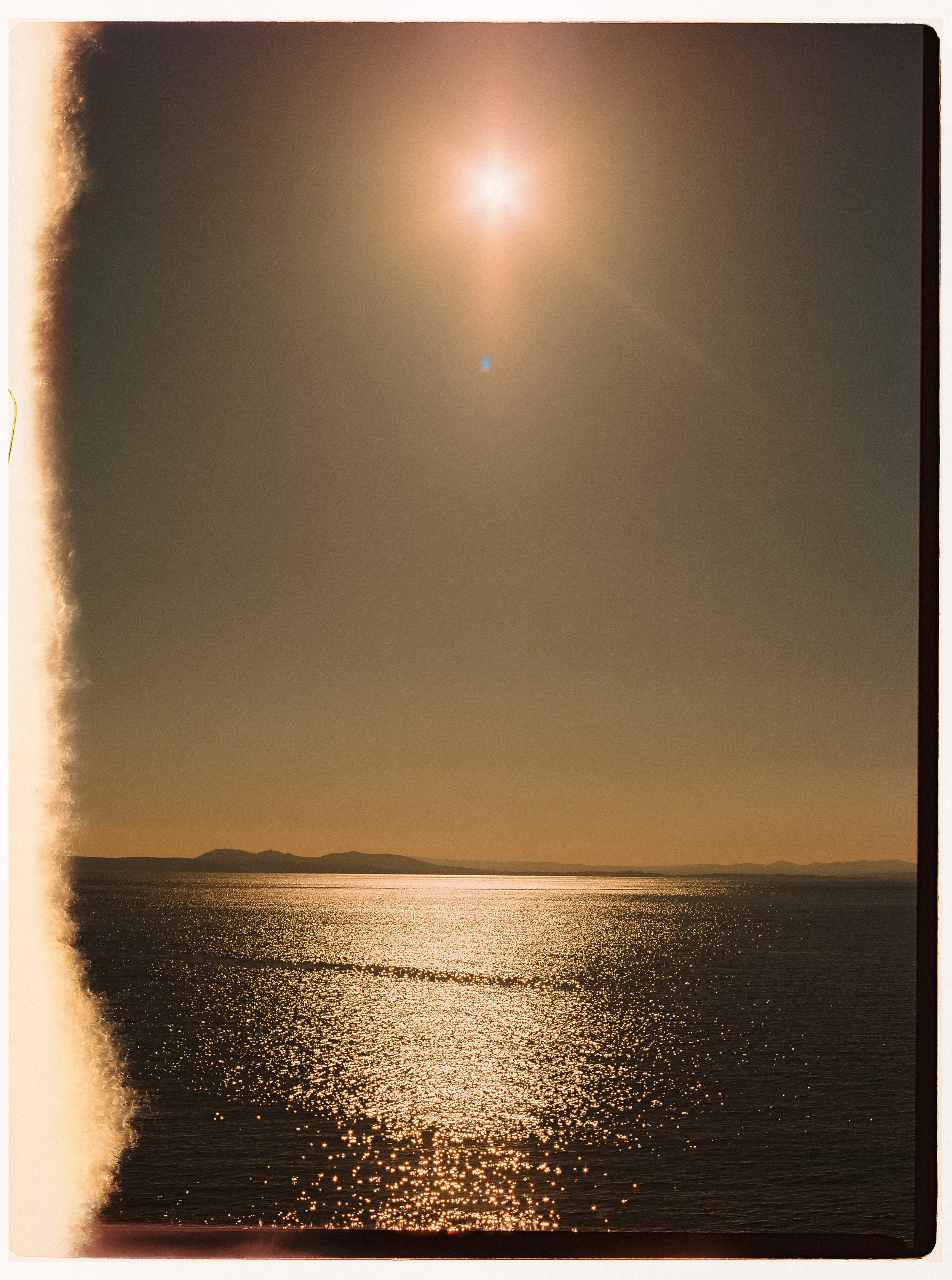 Una vista del mar al atardecer con el sol brillante en el cielo y el agua que refleja su brillo, con algunas islas en el horizonte.