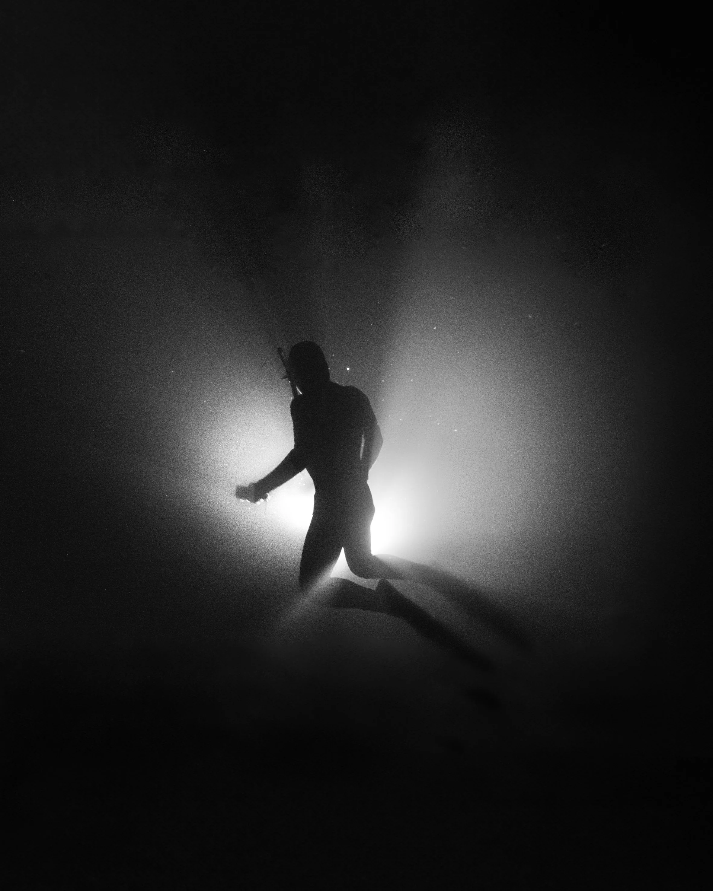 Silhueta de una persona con equipo de buceo en el agua en un entorno oscuro con luz brillante detrás.