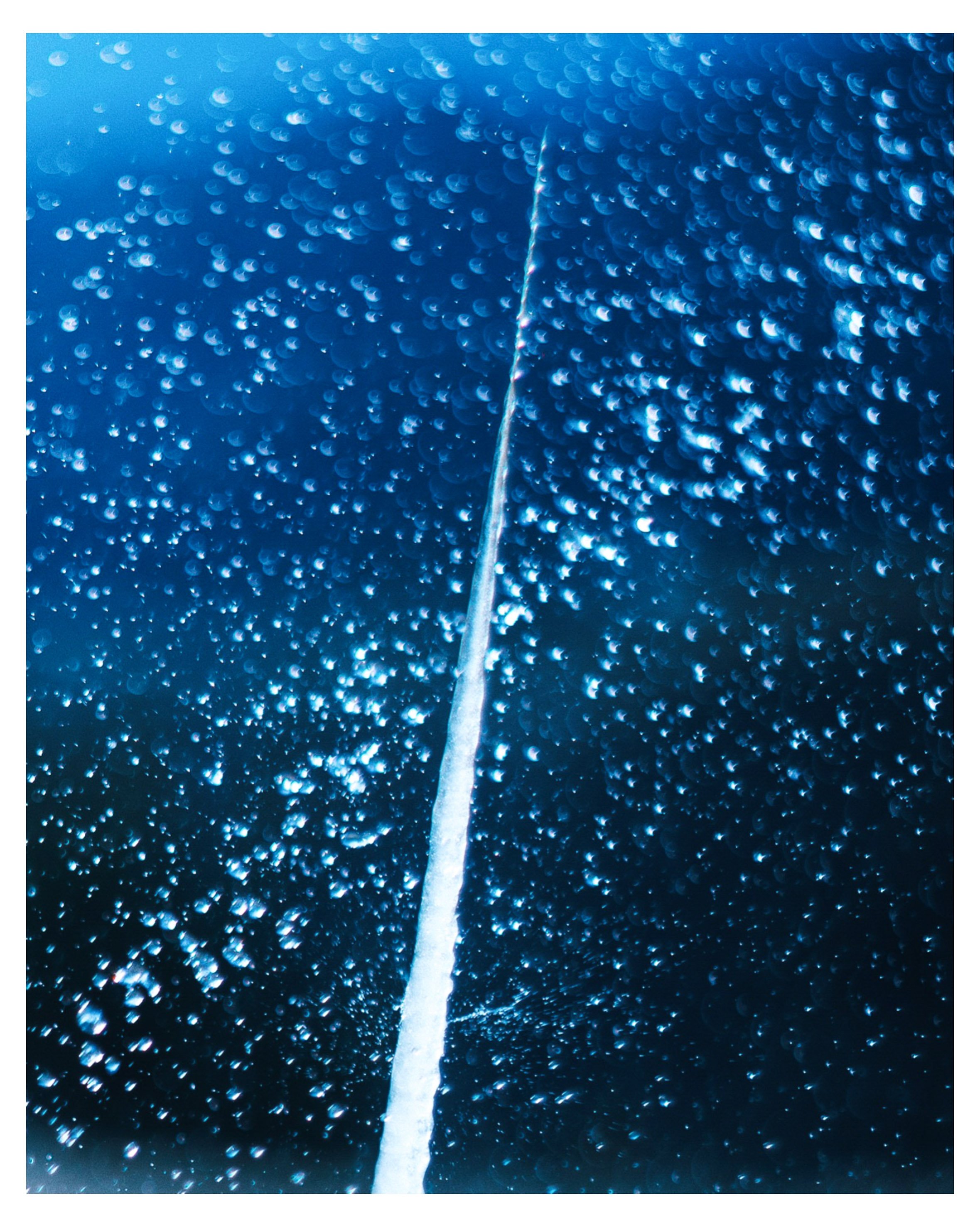 Vista desde el interior de un vehículo con gotas de agua en la ventana y una línea blanca en el centro.