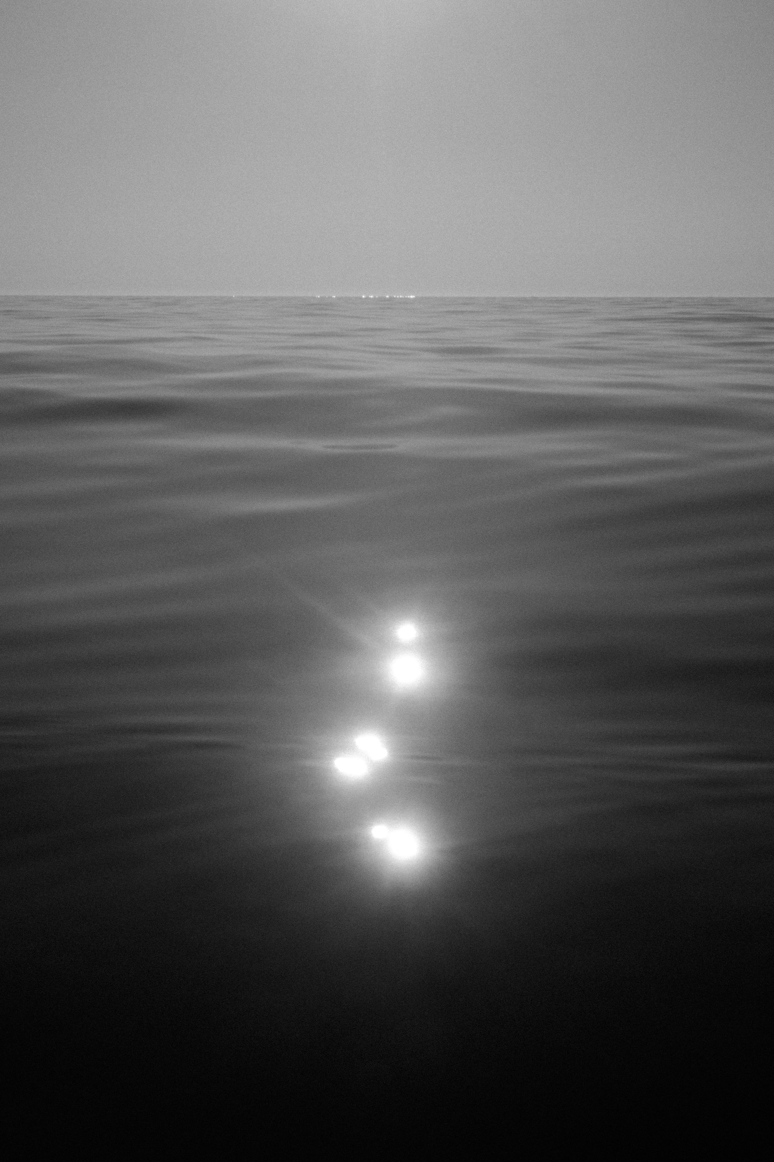 Mar abierto con reflejos del sol en el agua a lo lejos en escala de gris.