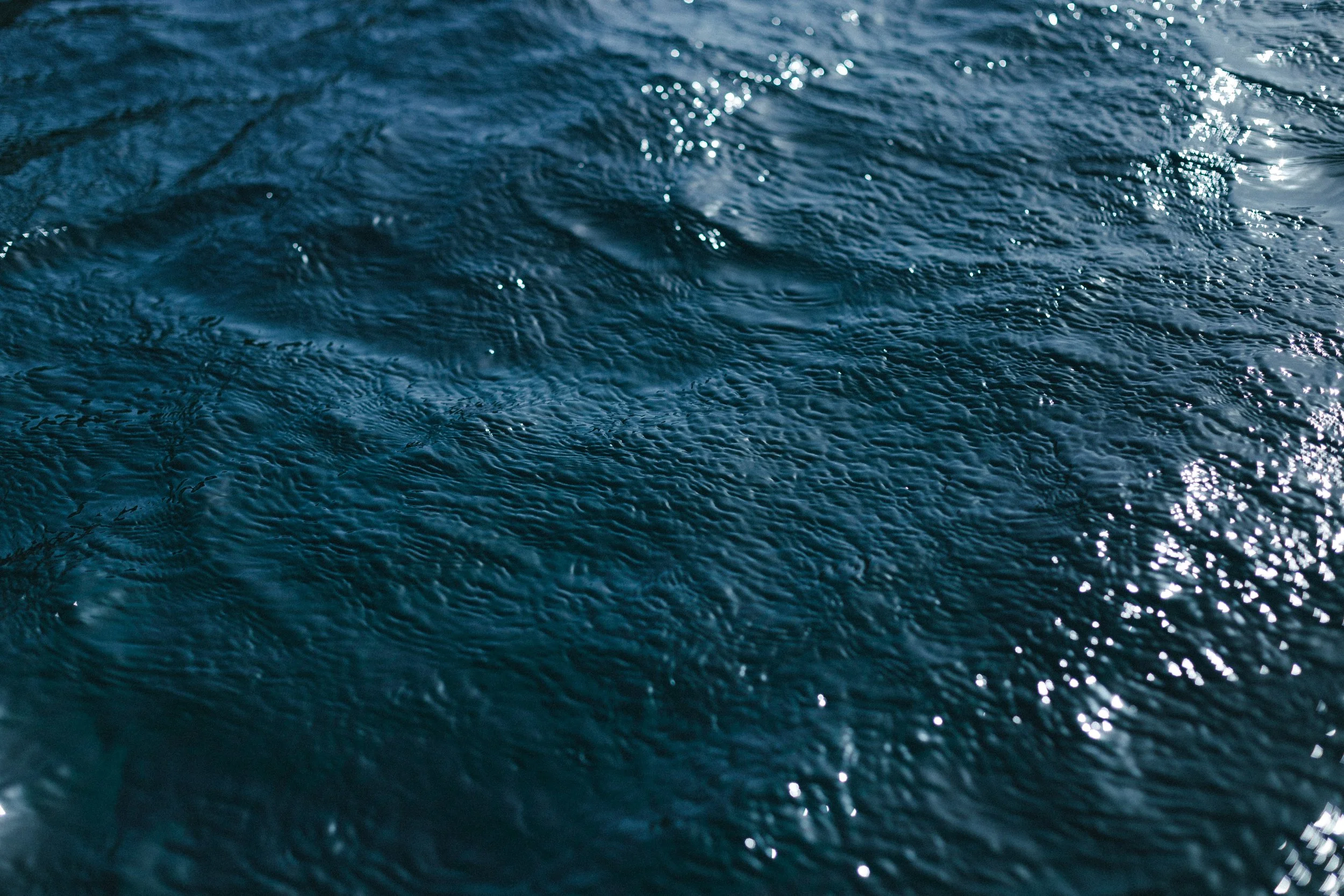 Superficie del agua del mar con olas y brillo del sol en la superficie.