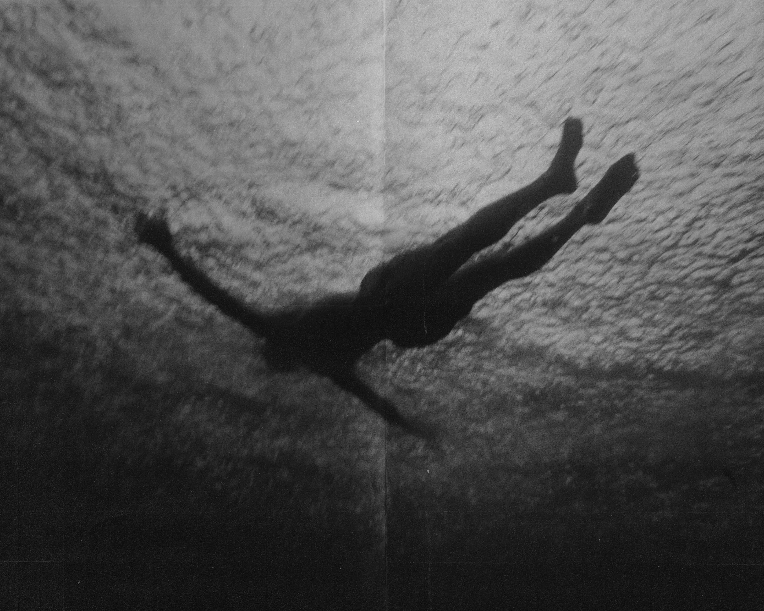 Persona nadando en el agua, vista en ángulo lateral, en blanco y negro.
