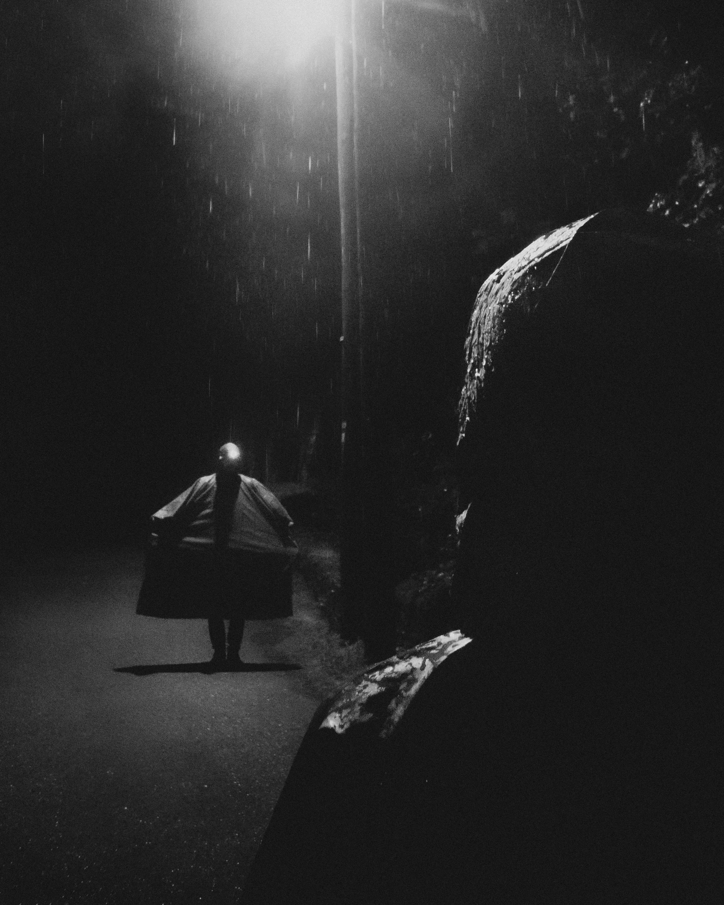 Una persona con paraguas en la noche lluviosa, iluminada por una farola, en un entorno oscuro y solitario.