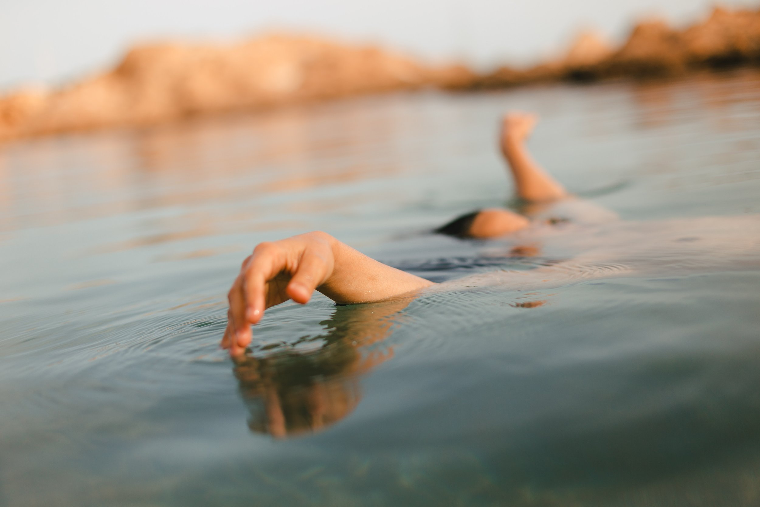 Persona nadando en un cuerpo de agua, vista de lado con brazo extendido y cabeza sumergida.