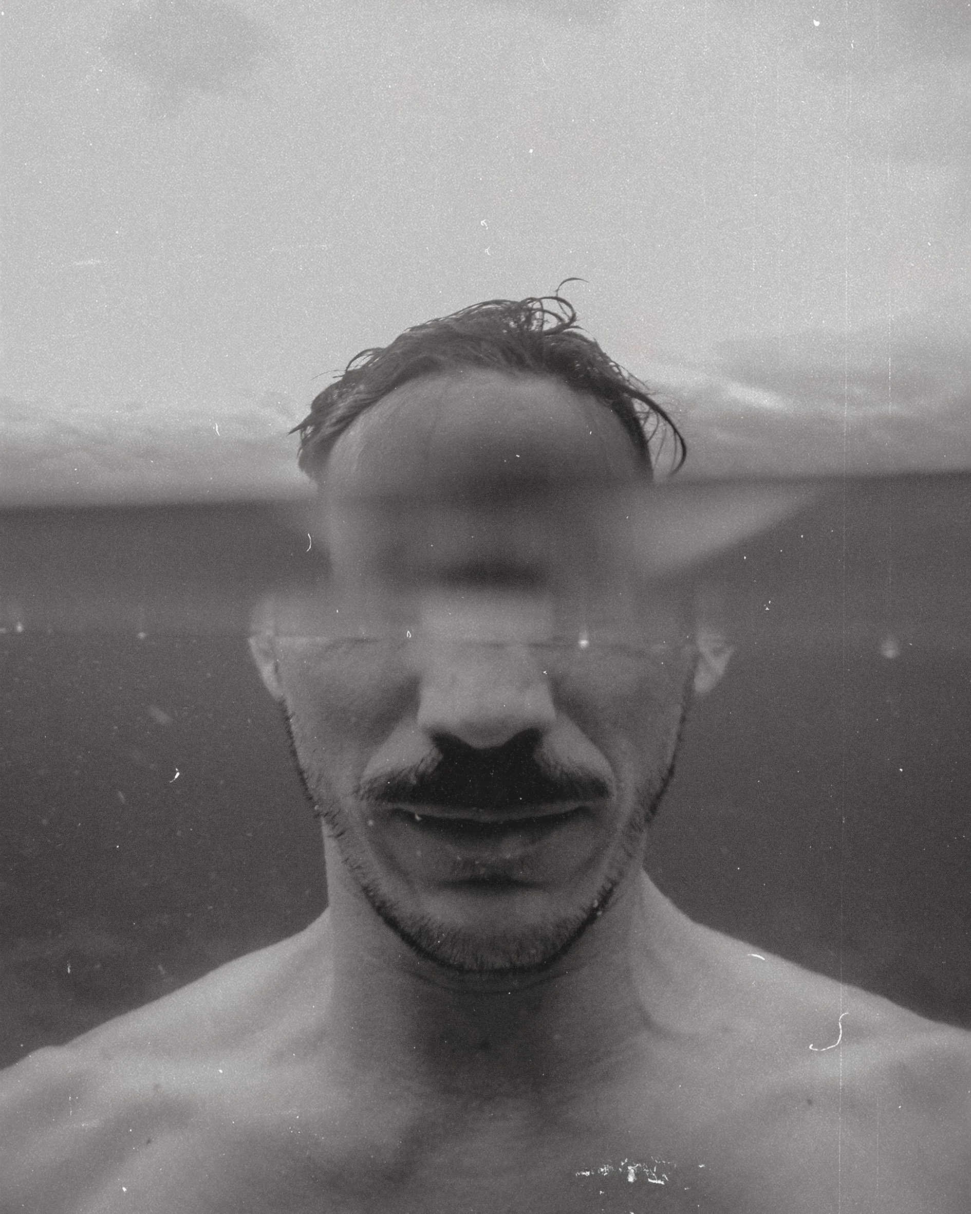 Hombre nadando en el agua con la cabeza parcialmente sumergida, vista en blanco y negro.