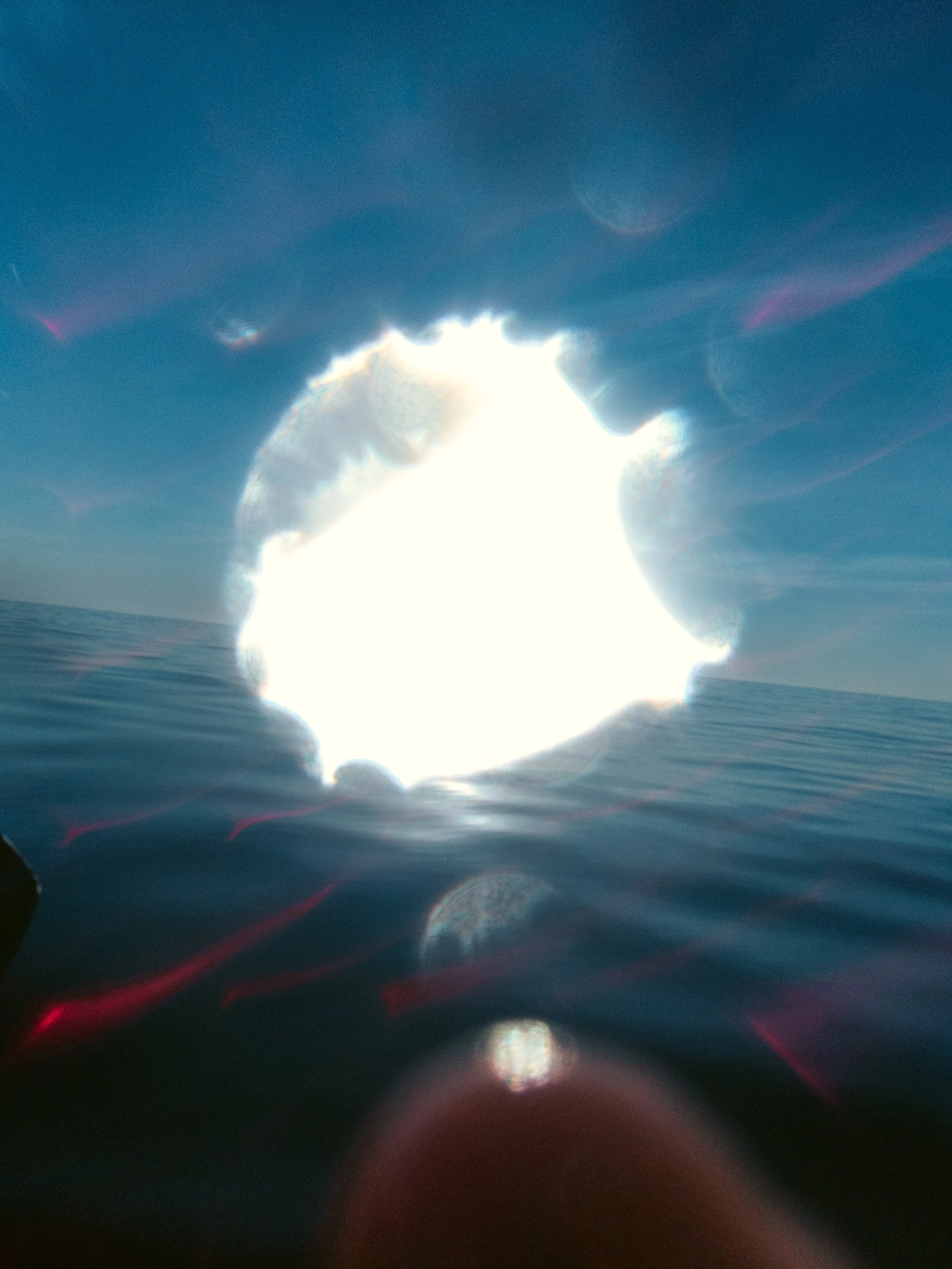 Foto de una puesta de sol en el mar, con reflejo en el agua, y un efecto de destellos y lentes. 