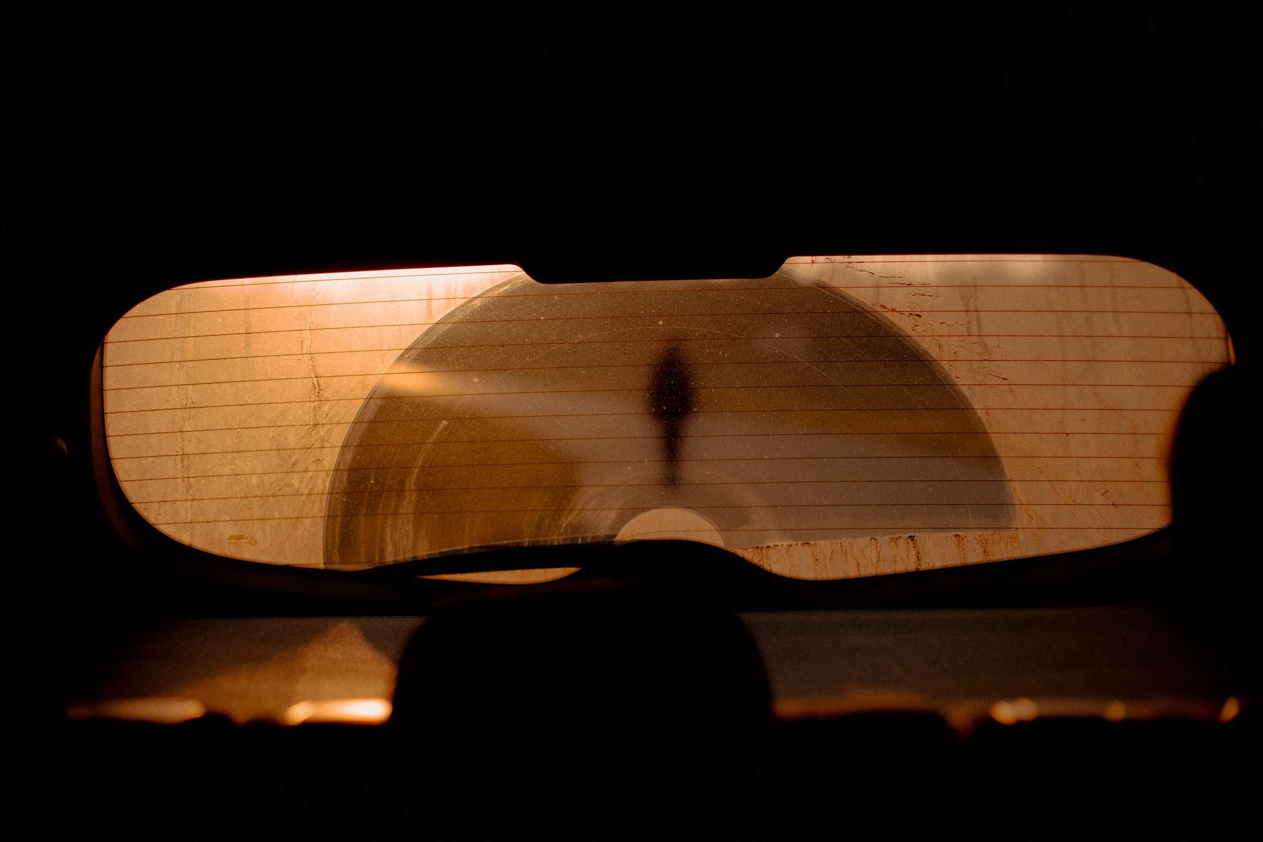 Vista desde dentro de un coche mirando hacia la parte trasera, con la luz del atardecer reflejada en el cristal de la ventana trasera