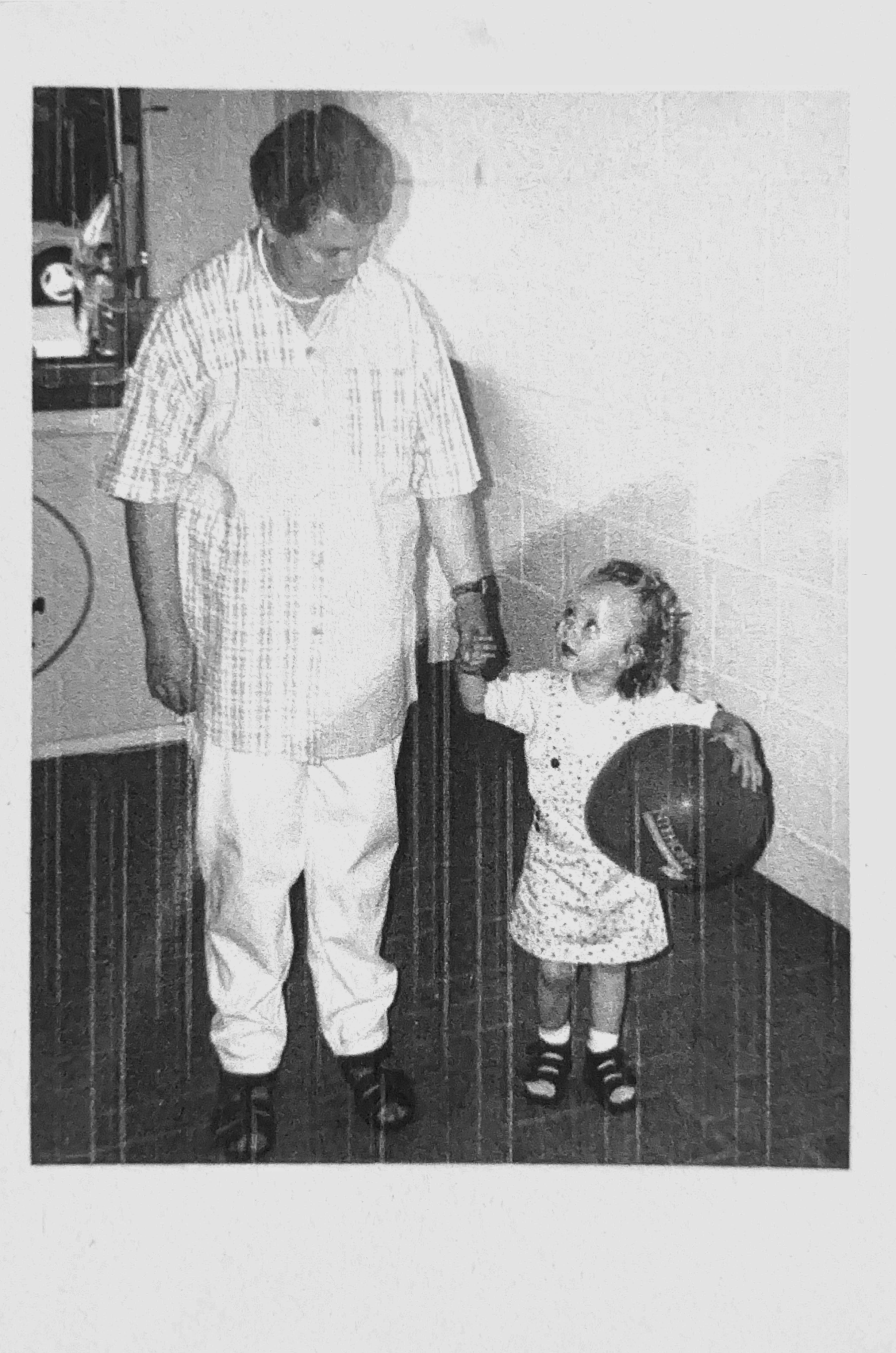 Ein Mann hält die Hand eines kleinen Mädchens, das einen Basketball und ein T-Shirt trägt.