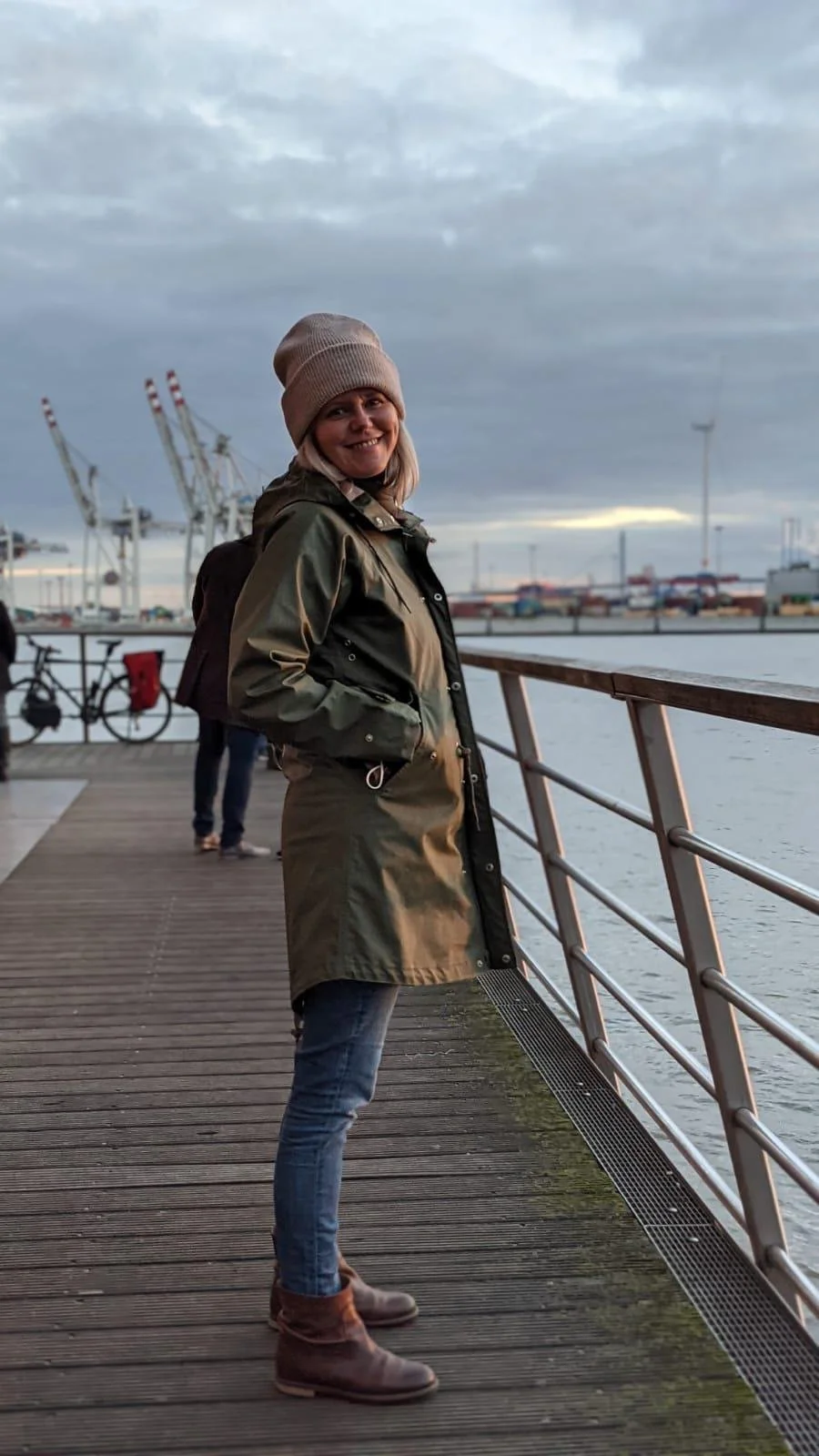 Frau im Outdoor-Jacken und Beanie am Hafen bei Sonnenuntergang