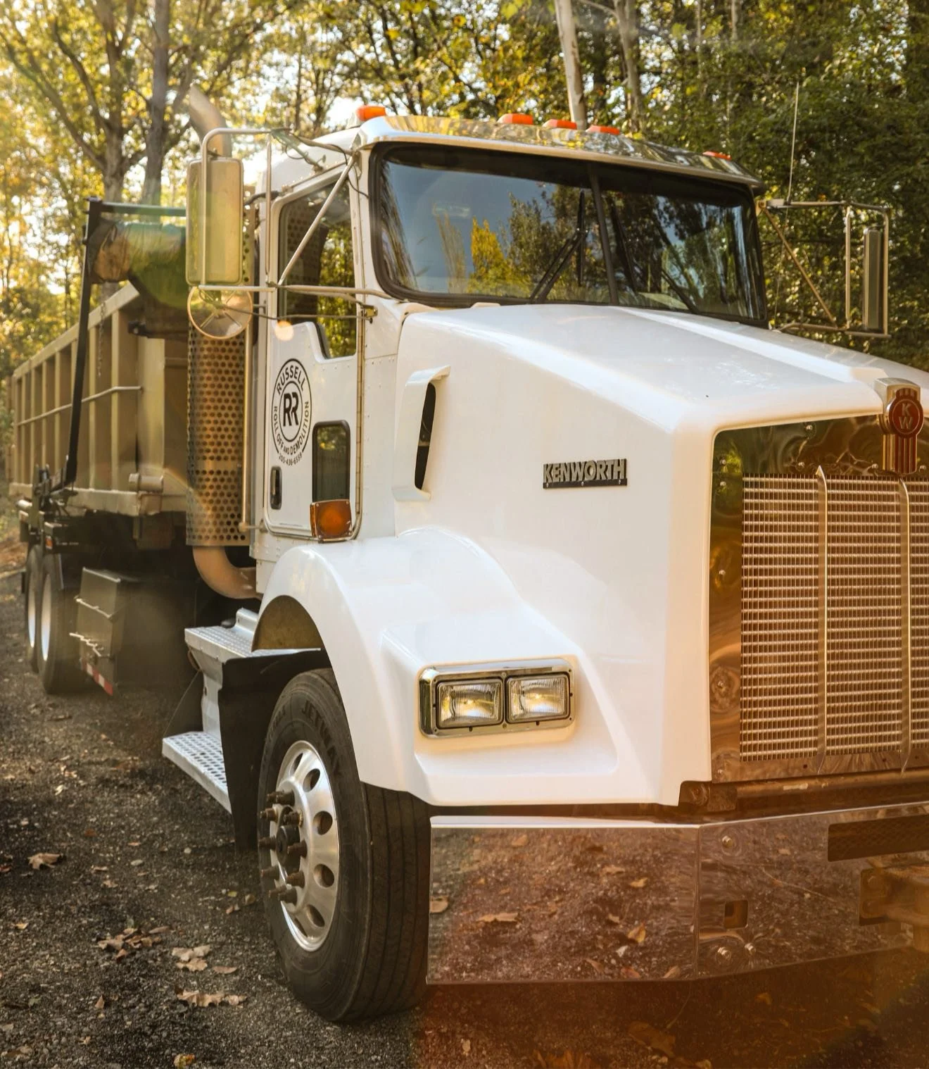 White Kenworth utility truck parked on a dirt road with trees in the background.