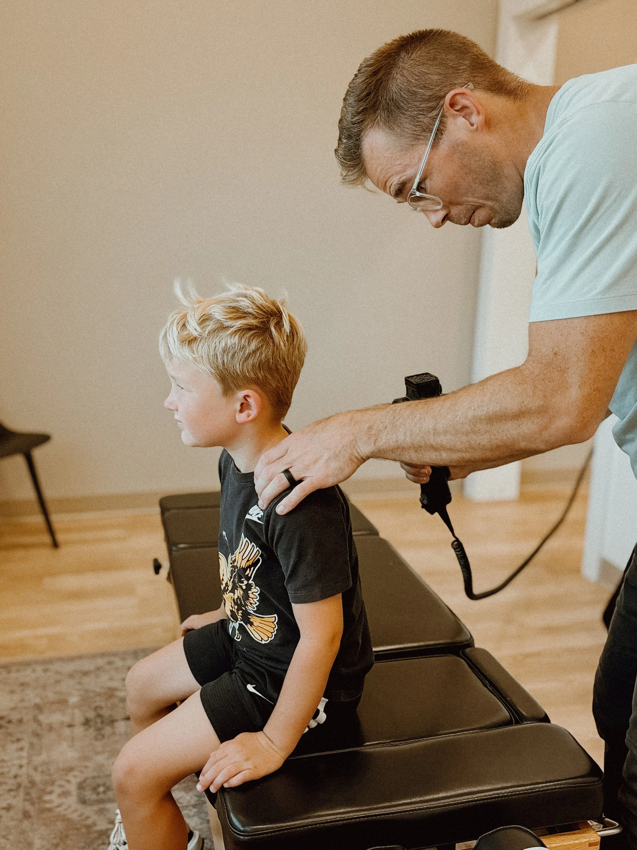 A young boy sitting on an examination table while a healthcare professional prepares to use an otoscope to examine his ear.