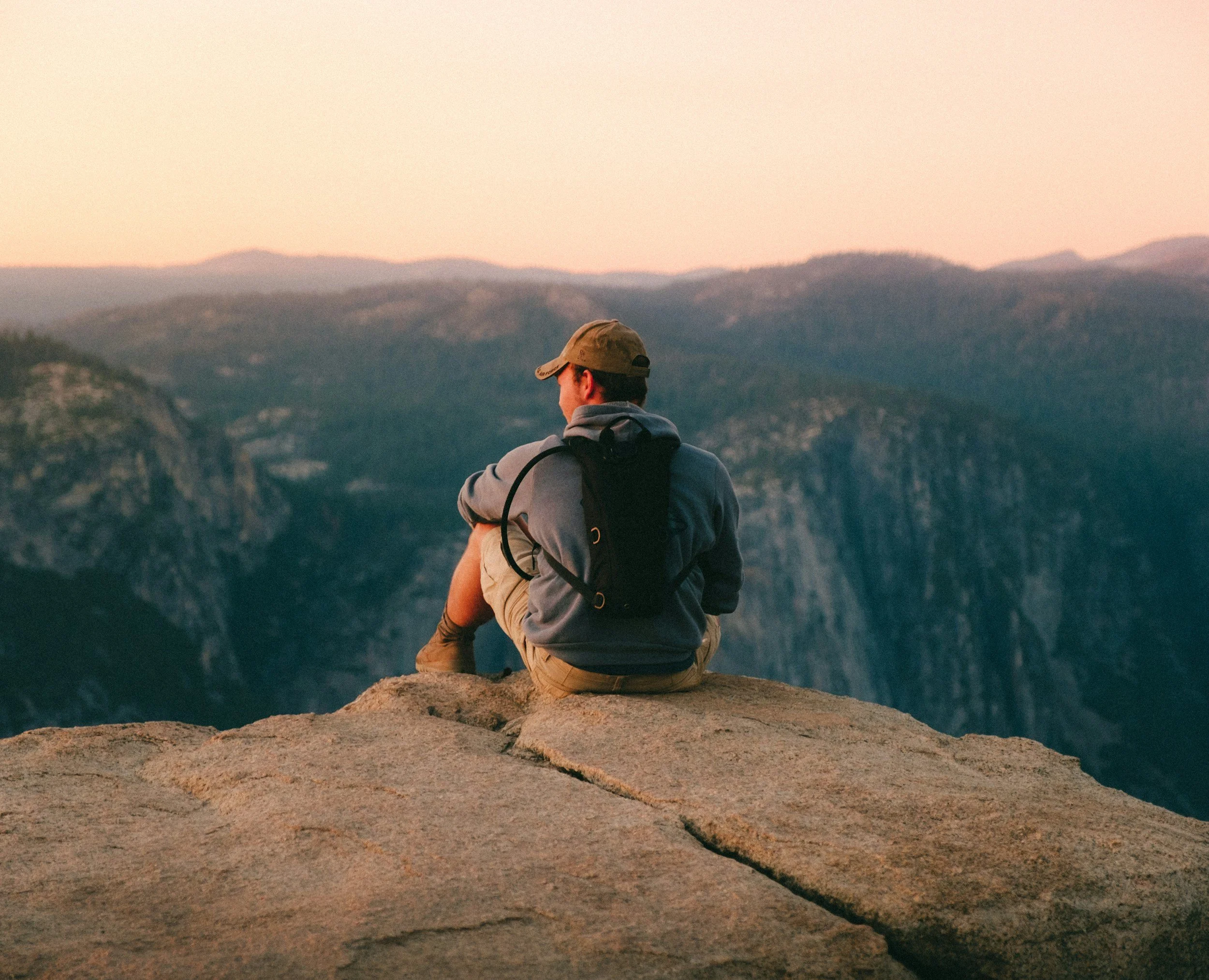 A man sitting at the top of a mountain at sunset while hiking