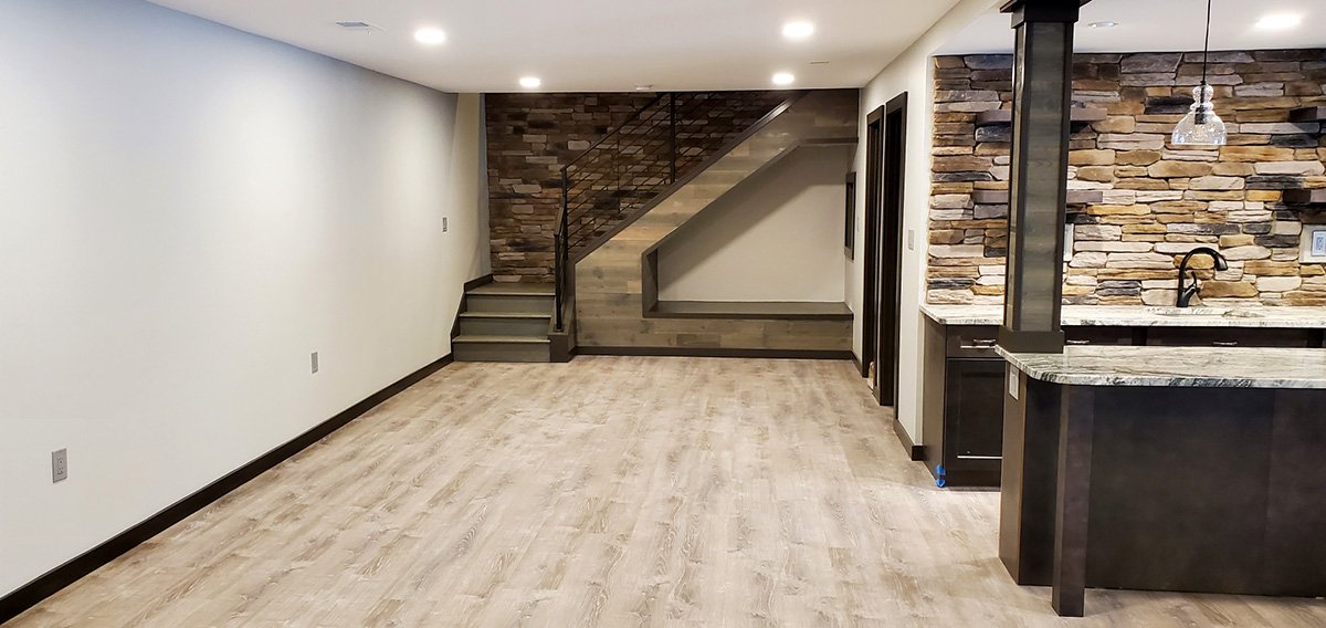 Empty living room with light wood flooring, white walls, and a staircase with a stone wall in the background.