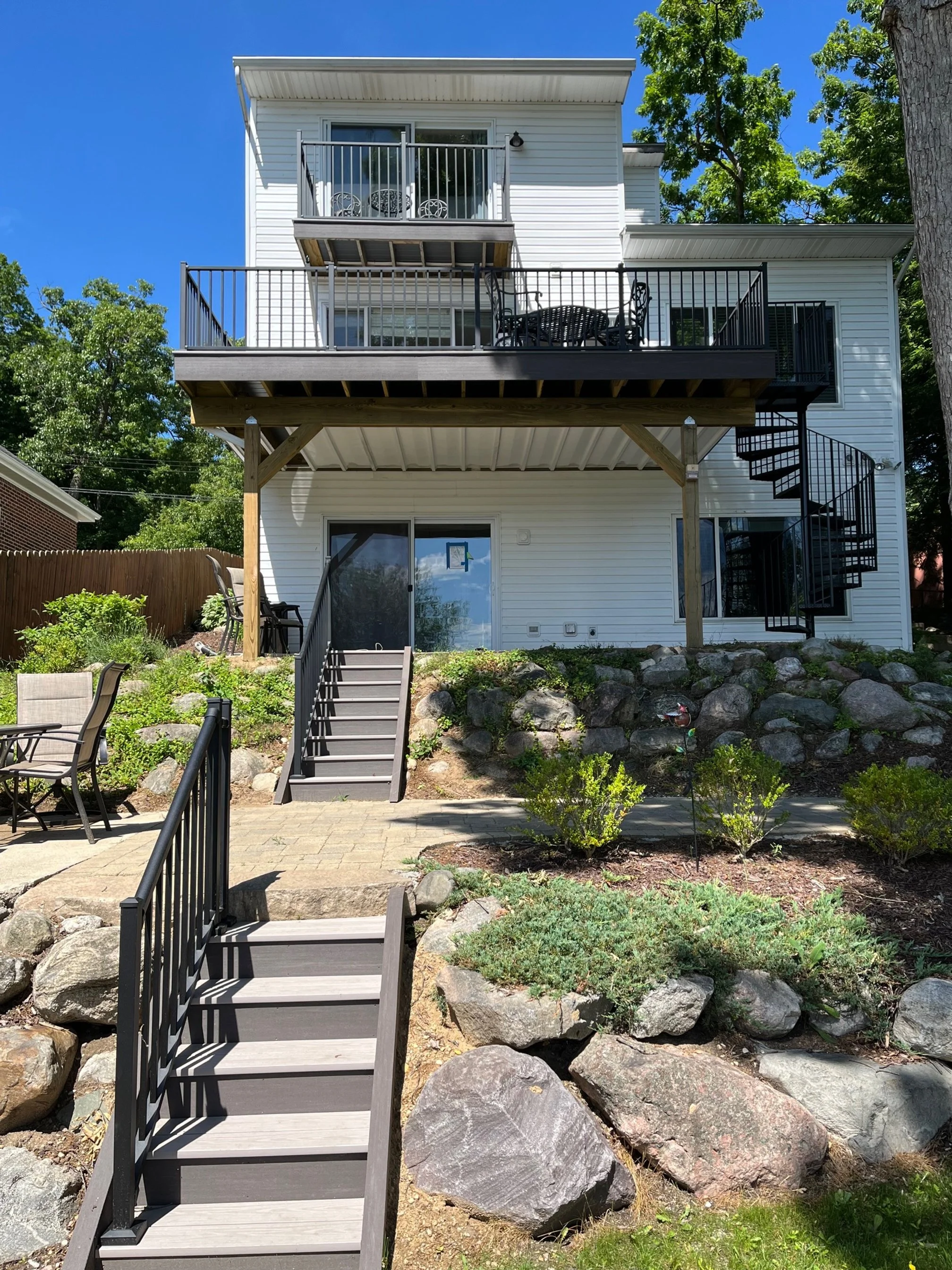 Backyard with stairs leading up to a house with two balconies, surrounded by rocks and greenery.