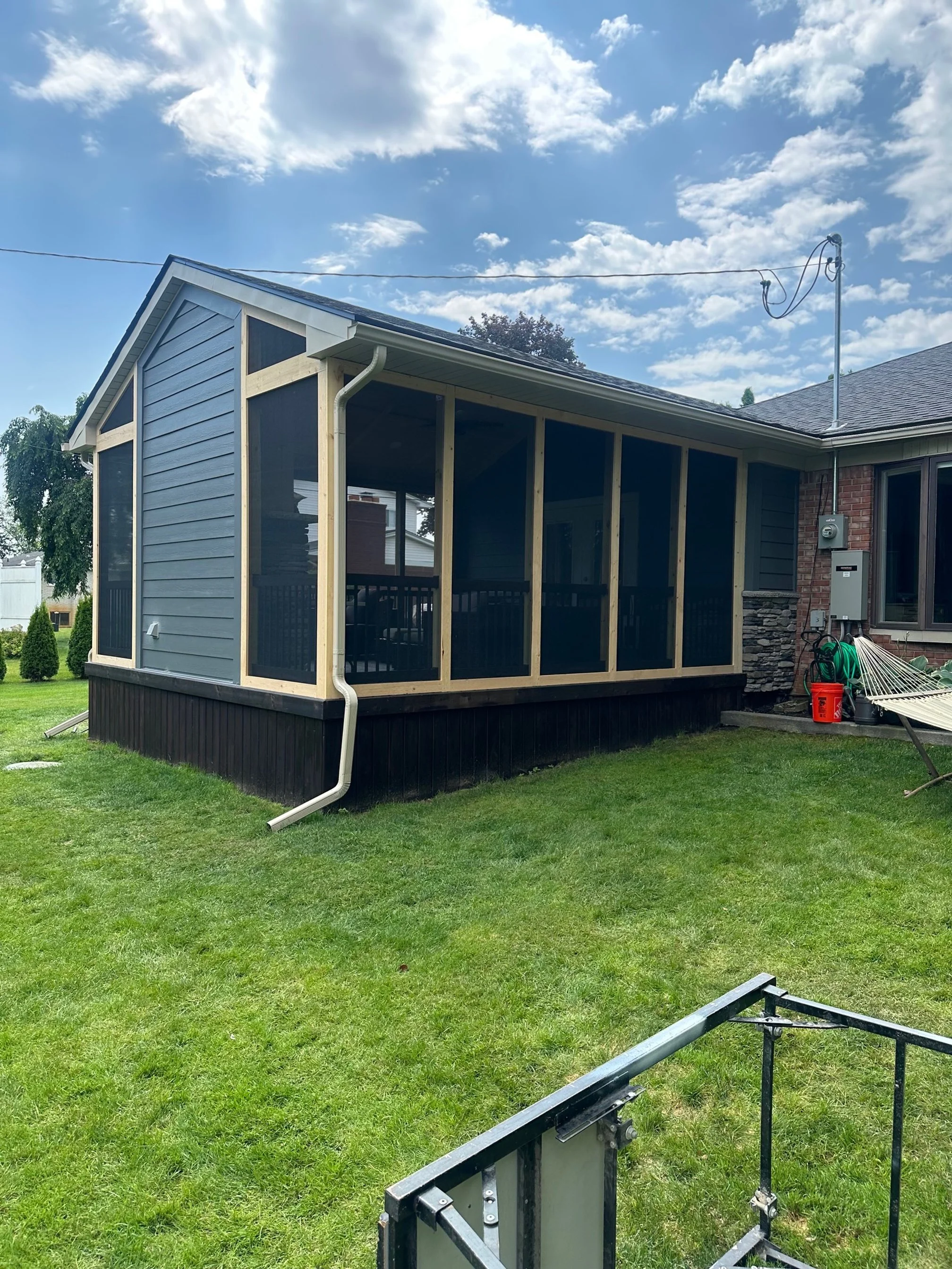 Backyard with a house featuring a screened-in porch under construction, a hammock on the grass, and a blue sky with clouds.