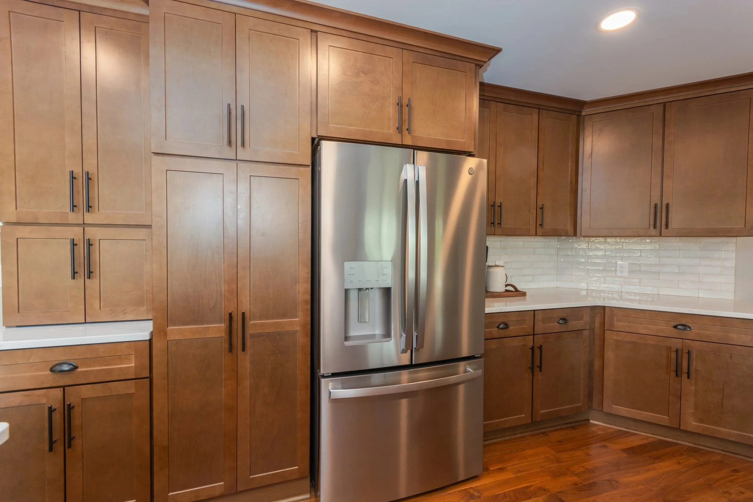 Kitchen with wooden cabinets, a stainless steel refrigerator, a white countertop, and a white brick backsplash.
