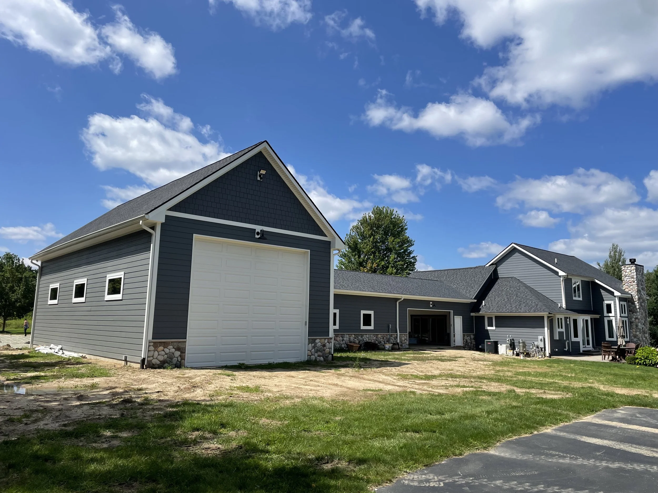 A new house with gray siding, a two-car garage, and a large lawn, under a bright blue sky with scattered white clouds.
