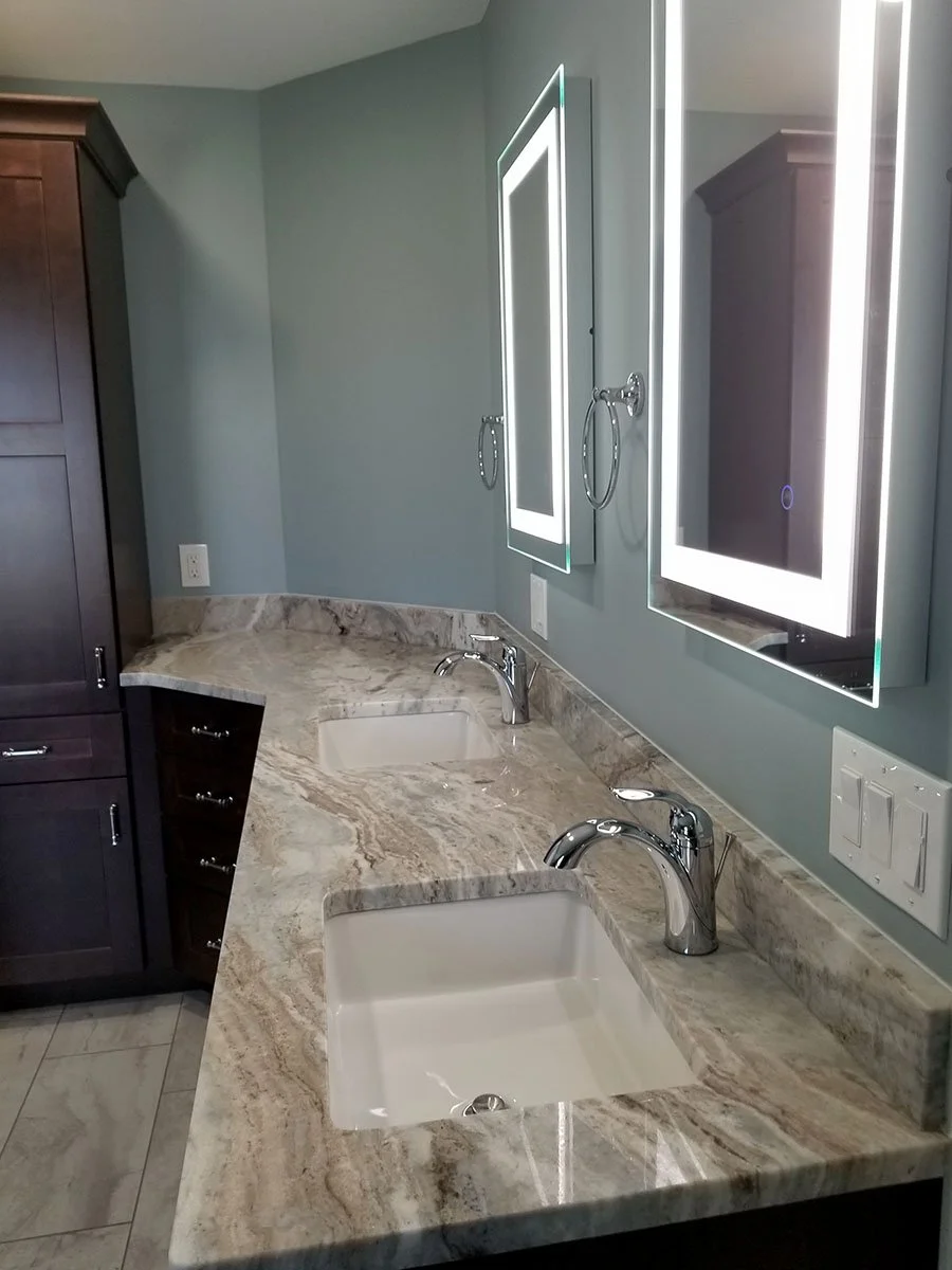 Bathroom vanity with dual sinks, marble countertop, illuminated medicine cabinets, mirrors, dark wooden cabinets, and modern fixtures.