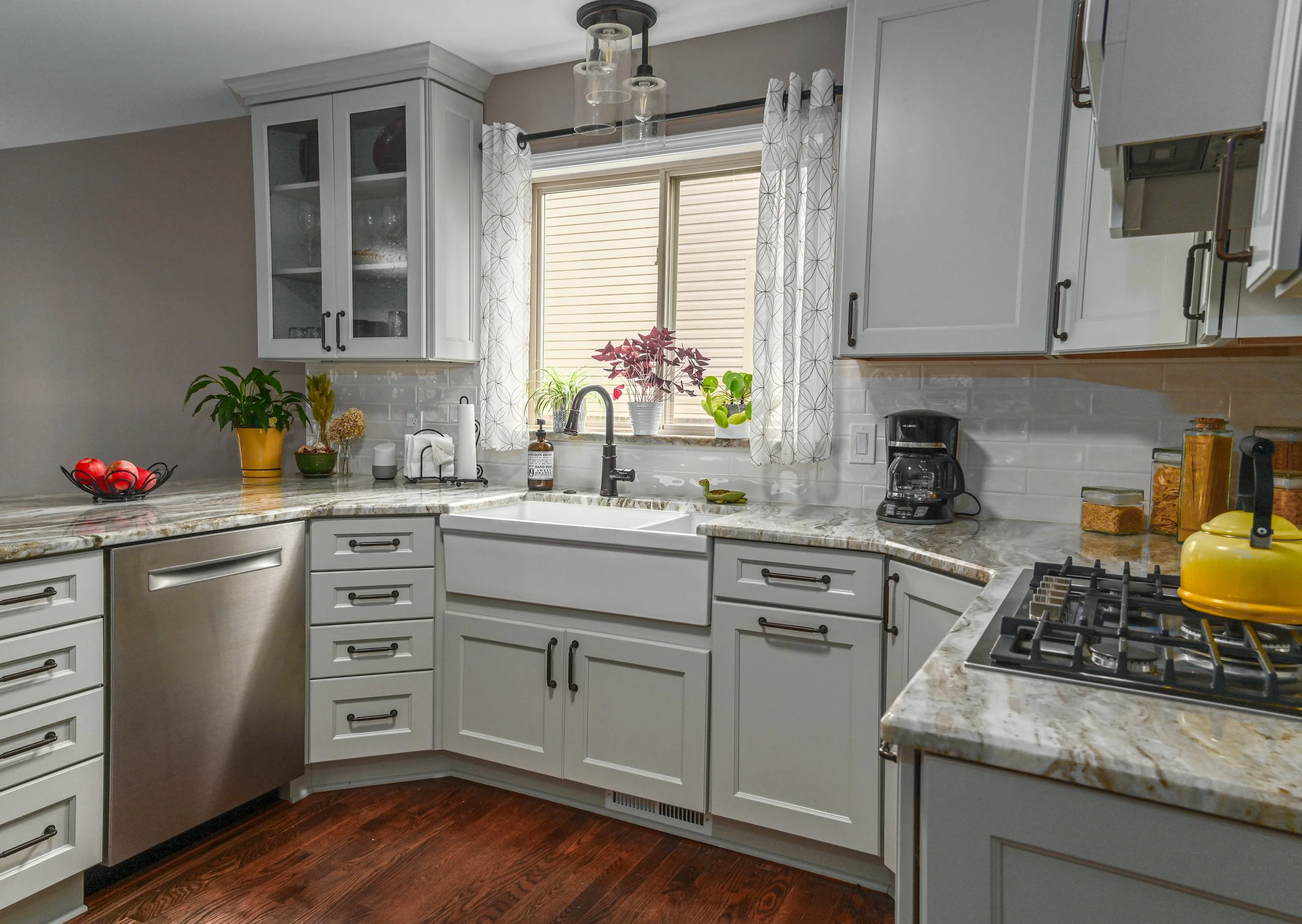 Kitchen with white cabinets, granite countertops, stainless steel dishwasher, coffee maker, yellow kettle, window above farmhouse sink, and various decorative items.