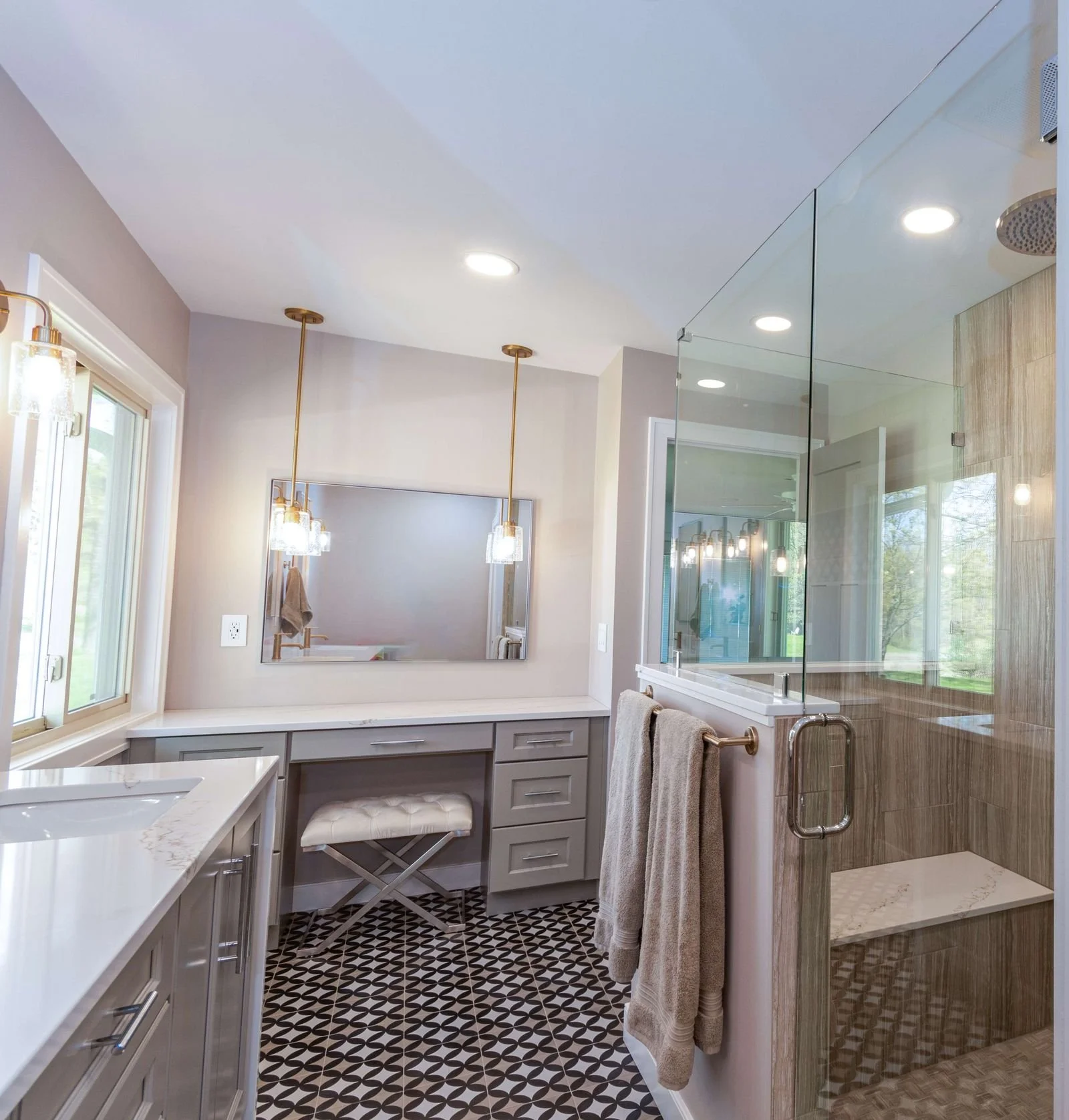 Modern bathroom with vanity area, mirror, pendant lights, and a glass-enclosed shower with wood-look tile.
