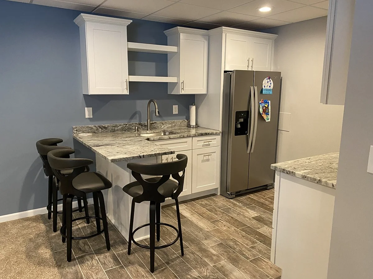Kitchen with white cabinets, stainless steel refrigerator, granite countertops, and four black bar stools at a breakfast counter.