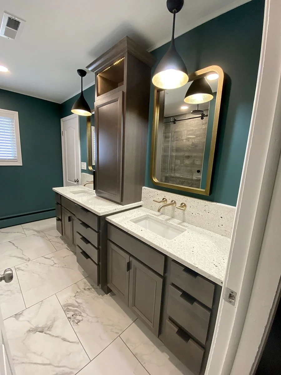 Bathroom vanity with dual sinks, a large mirror with a gold frame, teal walls, black pendant lights, a window with white blinds, a marble floor, and a wooden cabinet.