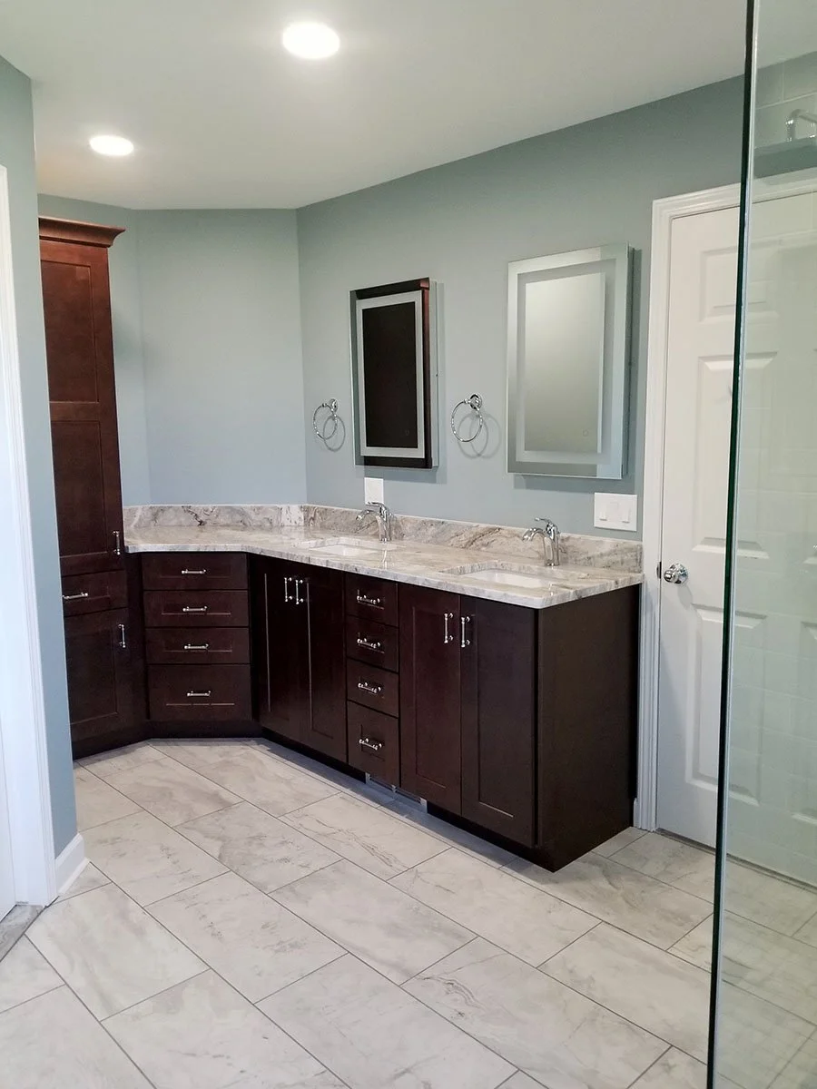 Modern bathroom with dark wood vanity, marble countertops, two mirrors, two sinks, and light gray walls.