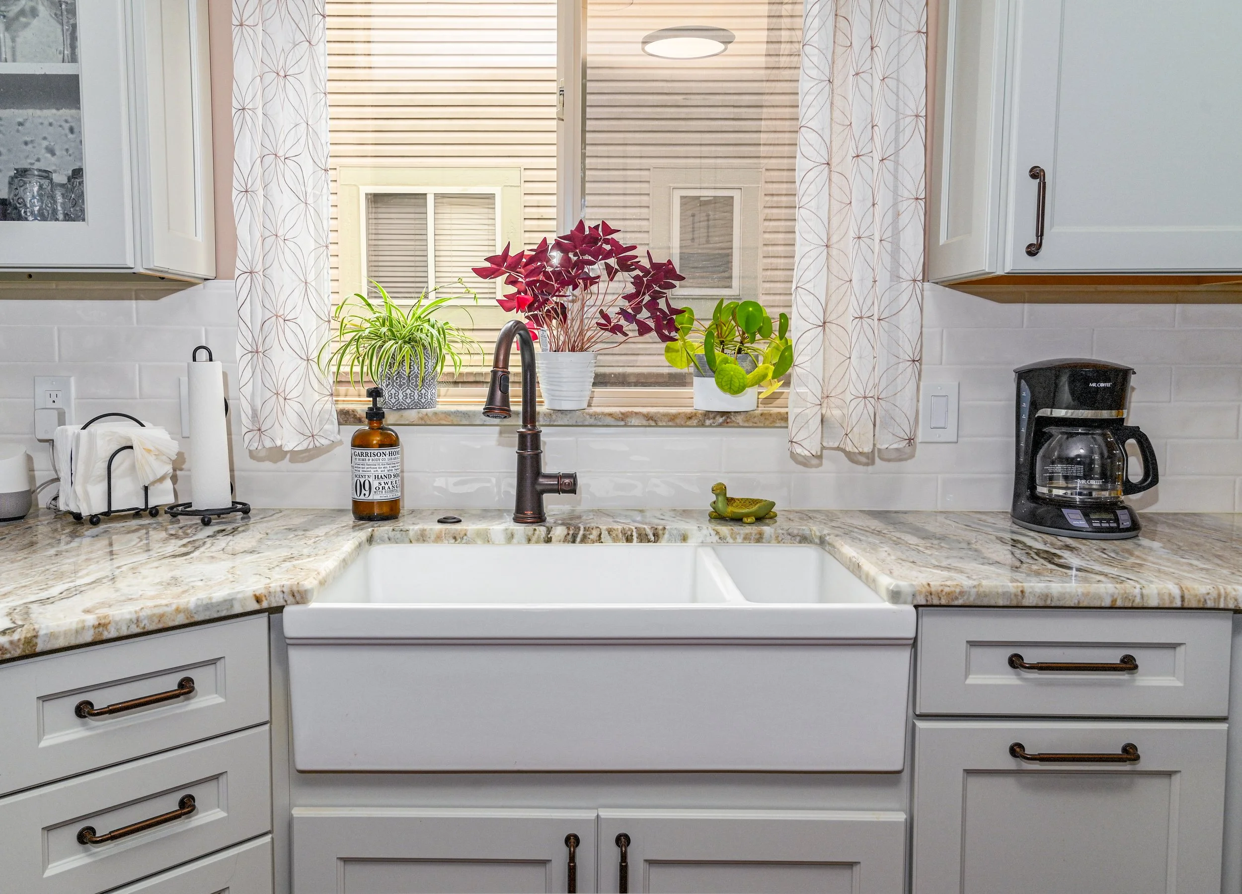 Kitchen sink with plants and a coffee maker on the marble countertop