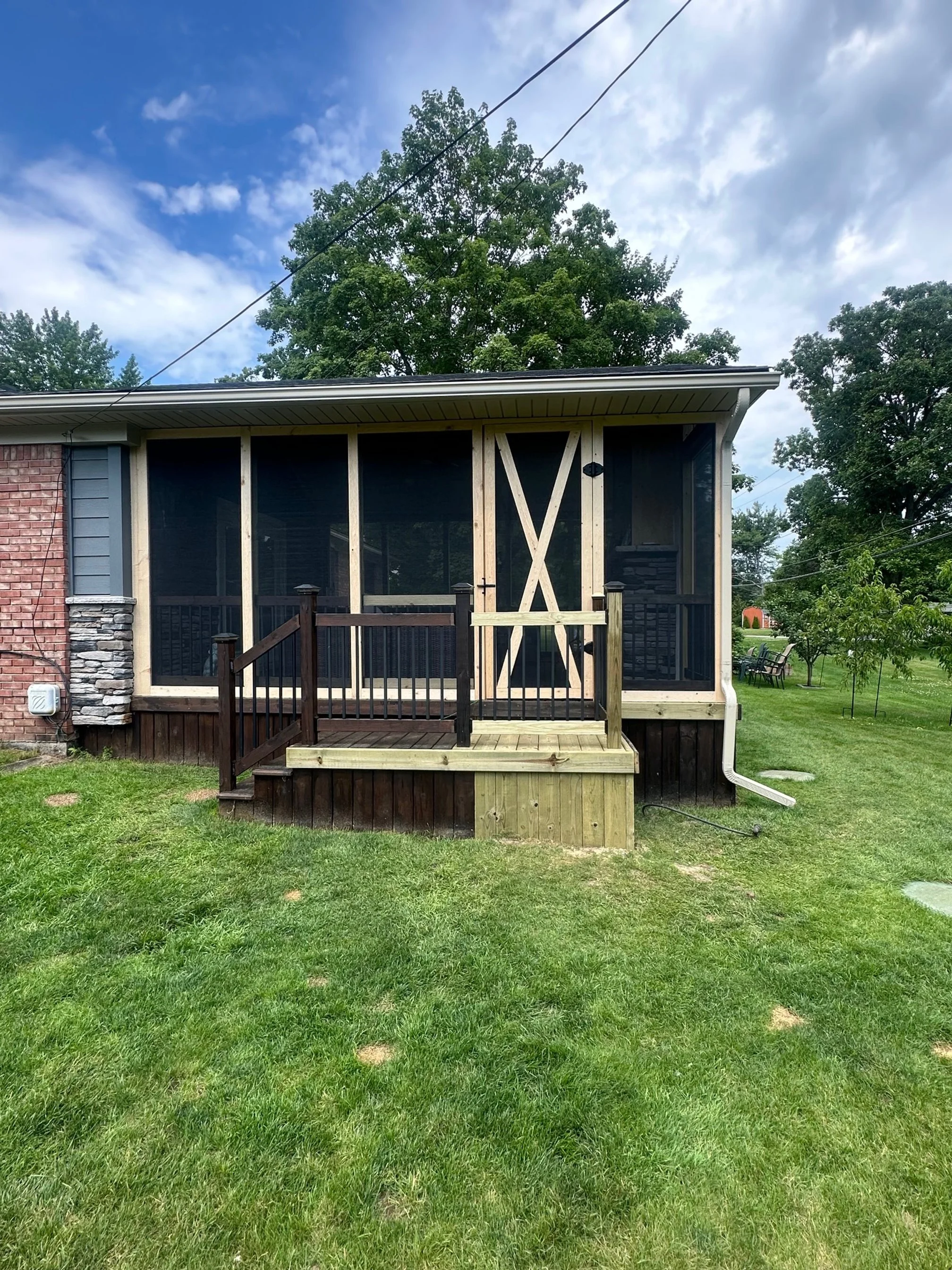 House with screened porch and new wooden stairs, green grass yard, trees, partly cloudy sky