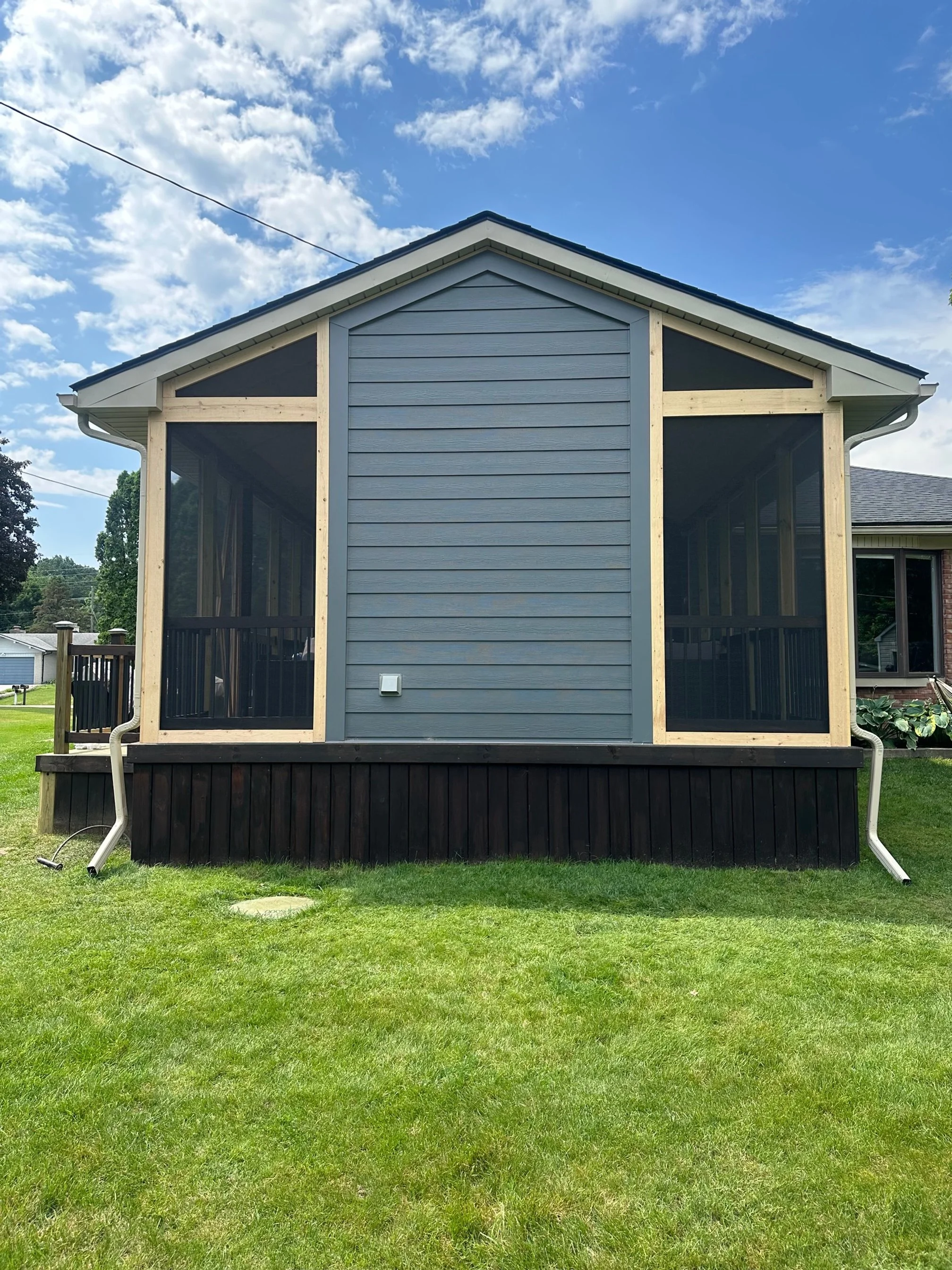 Back of a house with a screened porch, gray siding, black elevated foundation, and a clear blue sky.