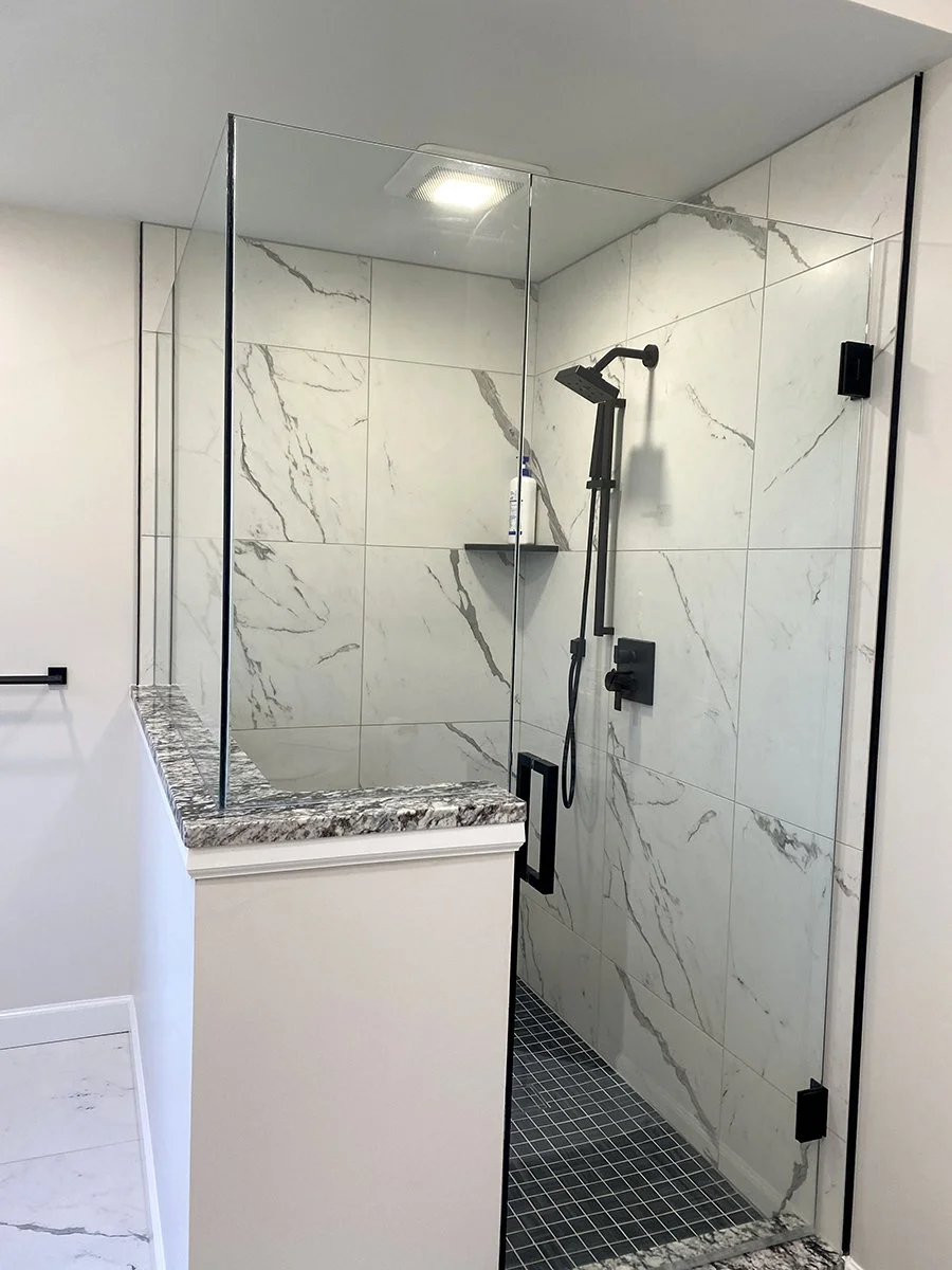 Bathroom shower with glass enclosure, marble tiles, black fixtures, and a built-in shelf.