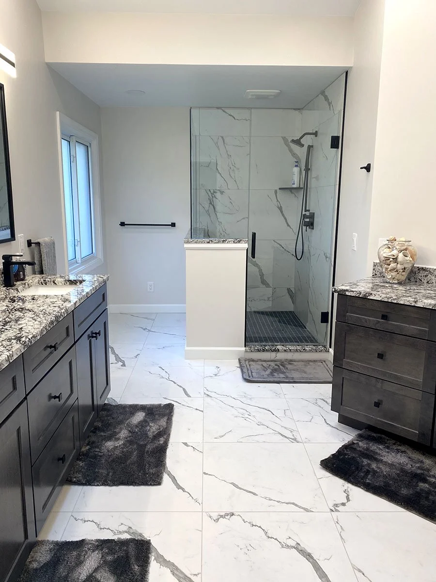 Modern bathroom with marble floor and shower, dark gray vanity, granite countertops, window, and black fixtures.