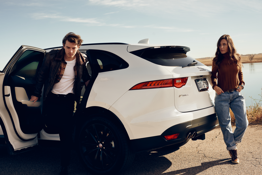 A man and a woman near a white car by a river in a rural setting.