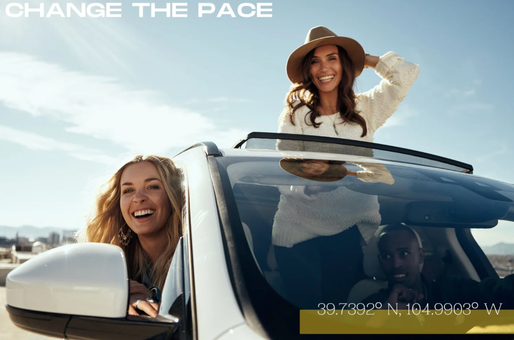 Two women and a man enjoying a ride in a car on a sunny day, with one woman standing through the sunroof and the other woman leaning out of the driver's side window. The scene is outdoors with a clear sky, and text overlay reading 'CHANGE THE PACE' in the top left corner, along with GPS coordinates at the bottom.