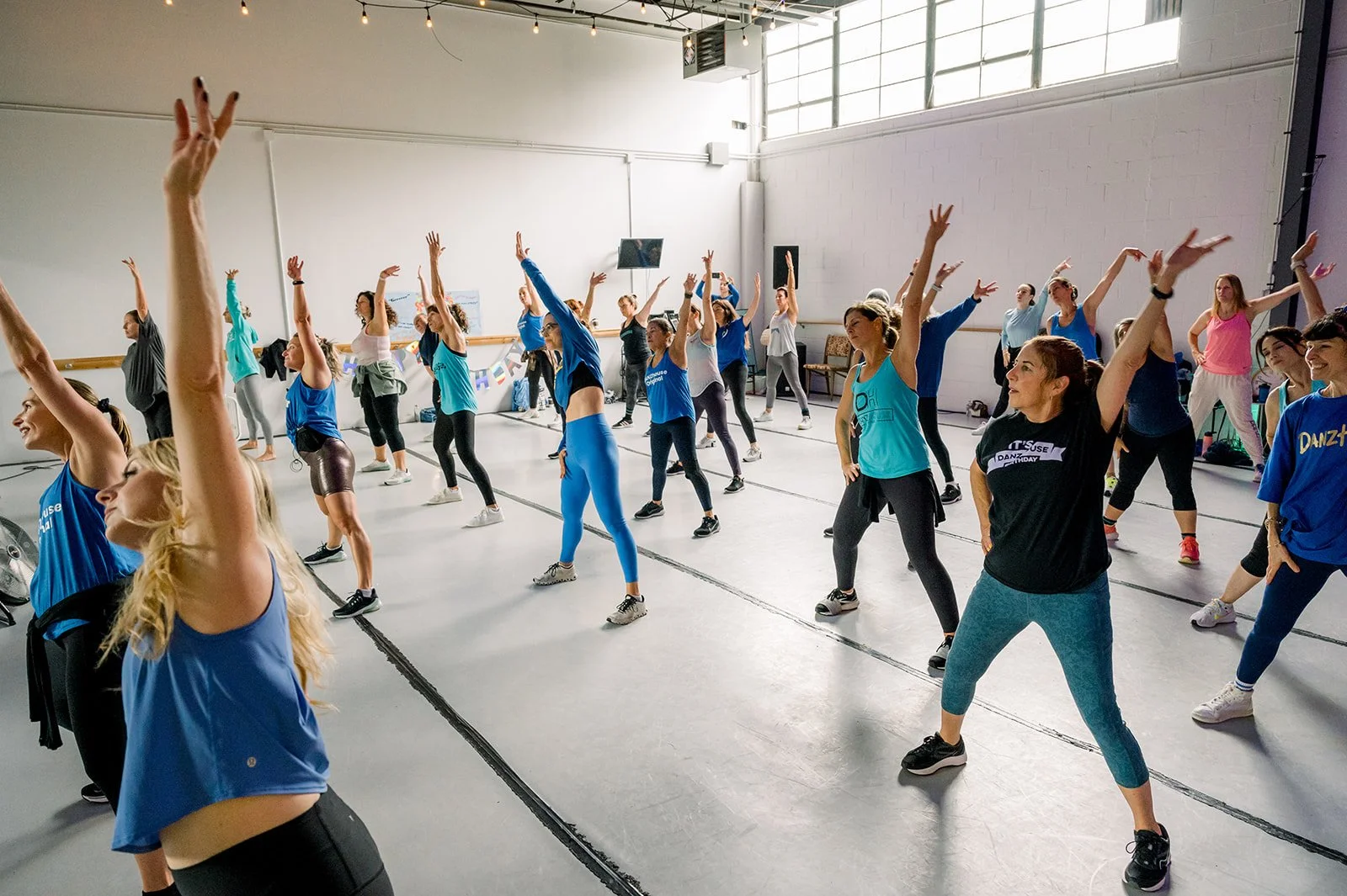 Group of women in a dance or fitness class doing stretching exercises in a studio with natural light.