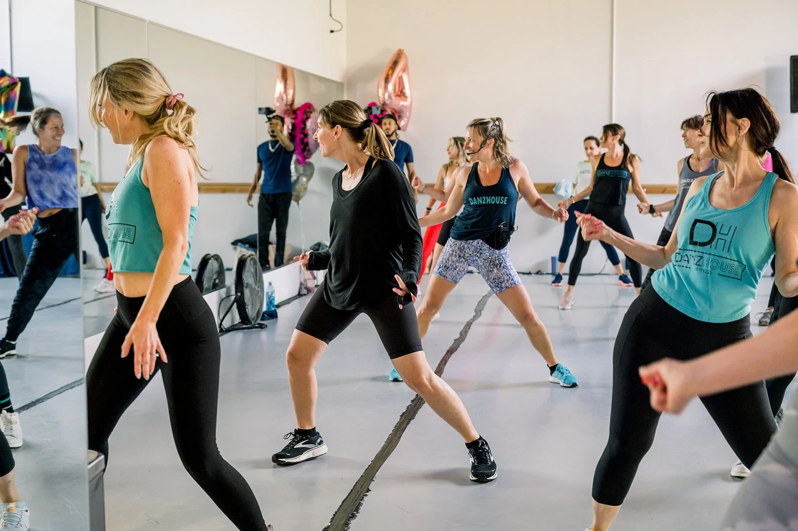 Women participating in an indoor dance fitness class, dancing with their arms extended and smiling.