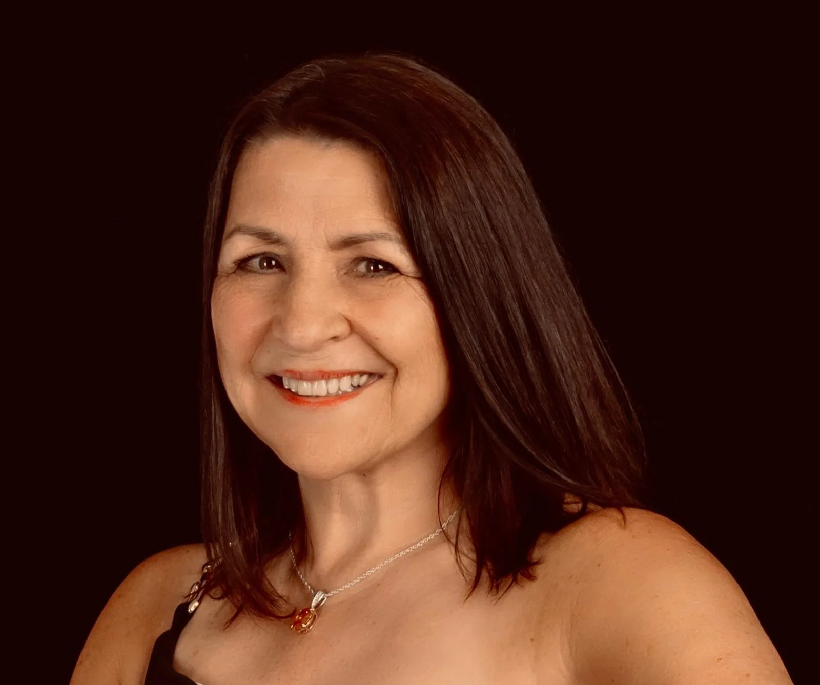 A smiling woman with medium-length brown hair, wearing a black top and a silver necklace, against a dark background.